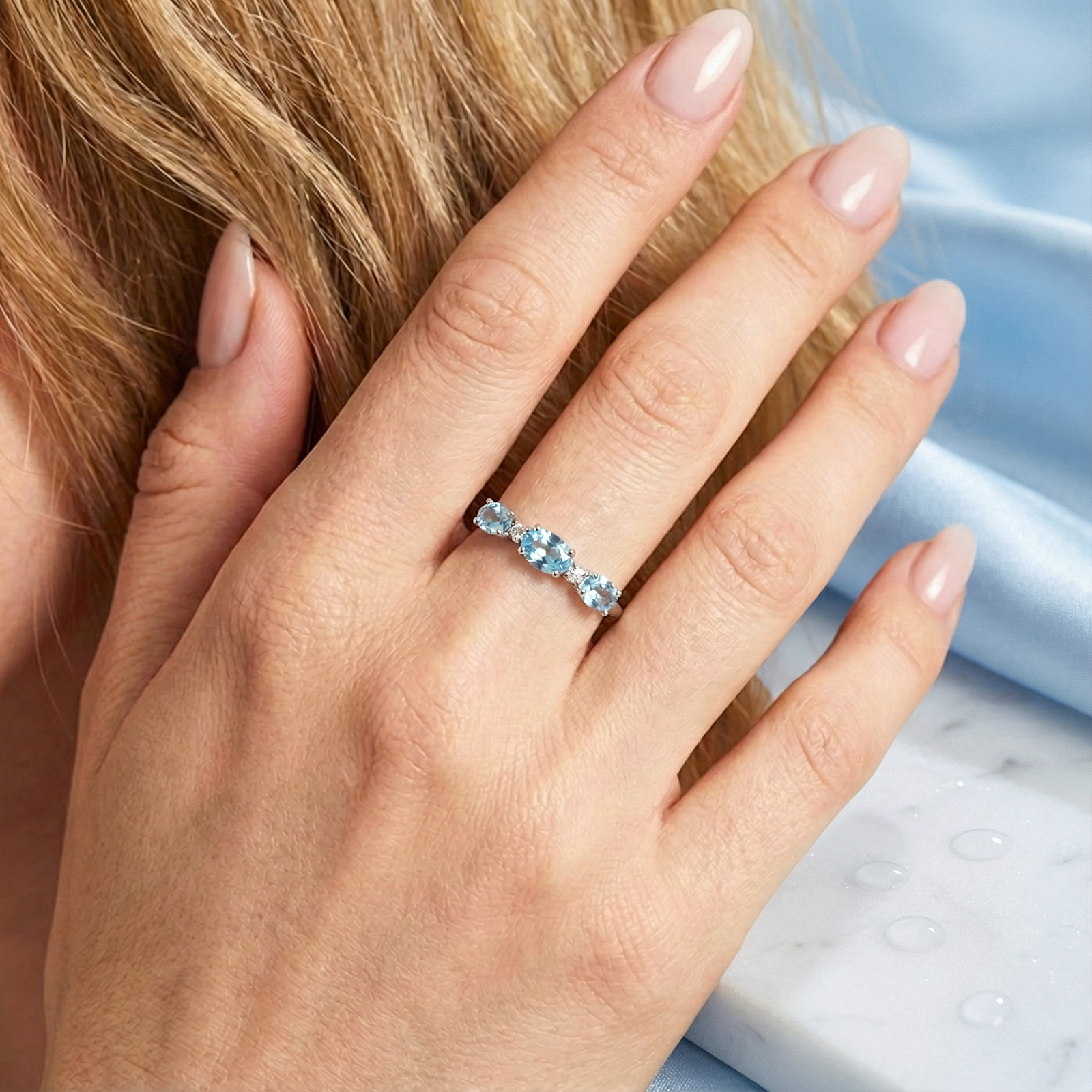 Close-up of the S925 sterling silver Maris bypass ring with oval simulated aquamarines on a woman's finger.