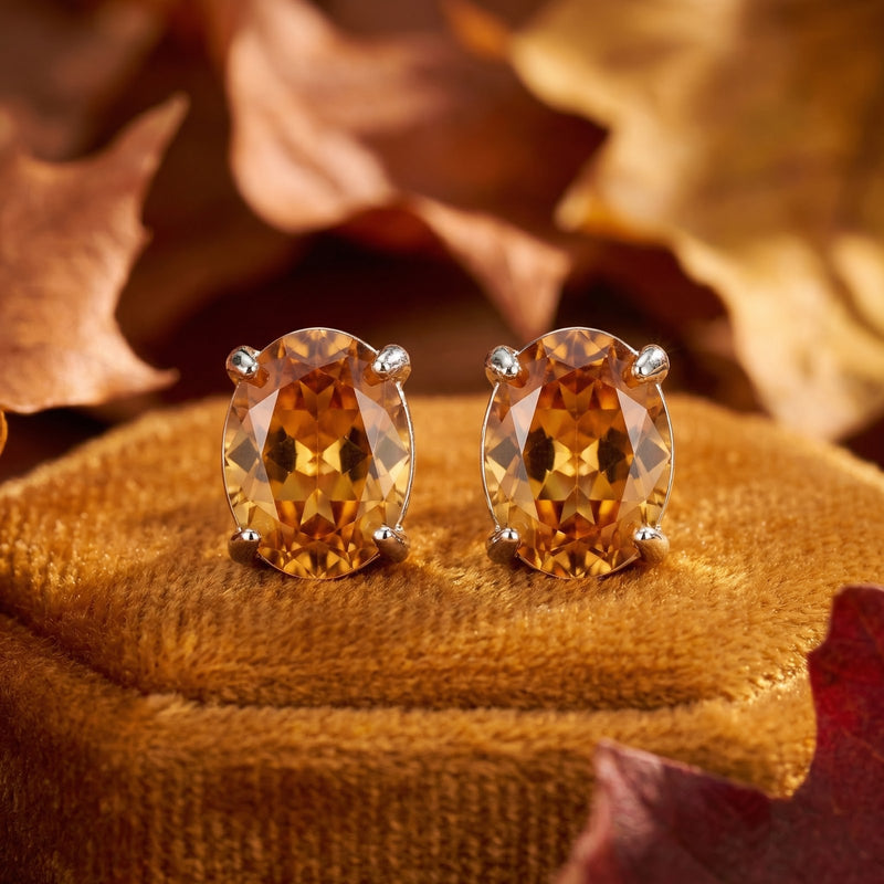 Macro view of oval cut honeyed simulated topaz stud earrings in silver four-prong settings.