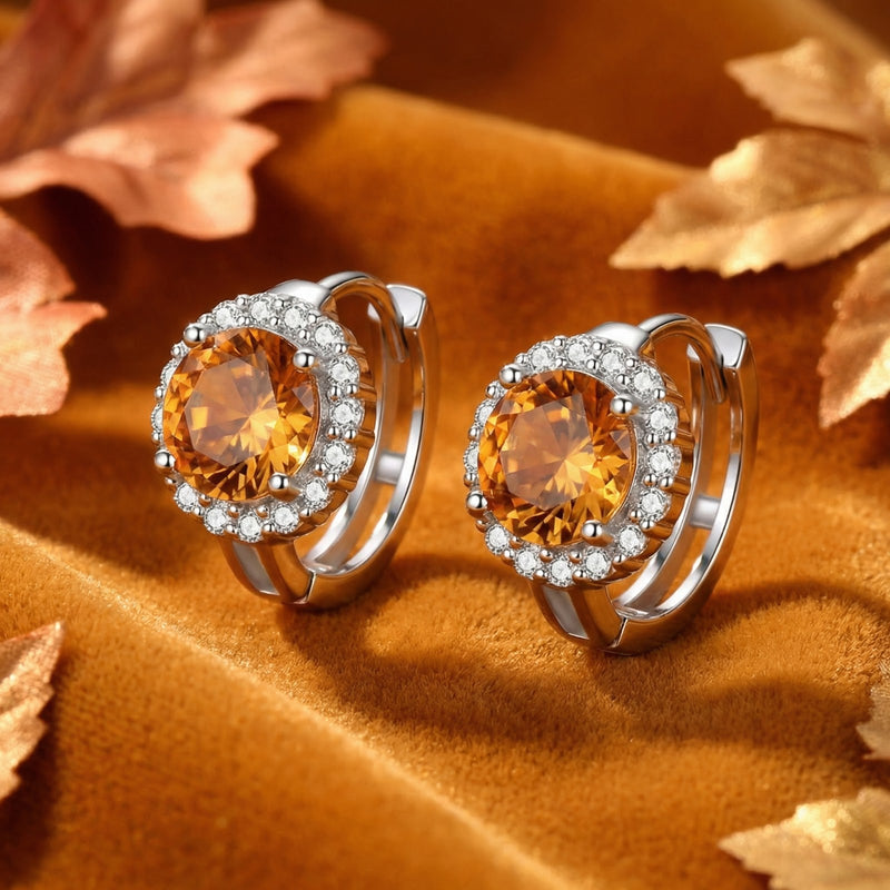 Sterling silver huggie hoop earrings with round honey moissanite halo settings on an autumn background.