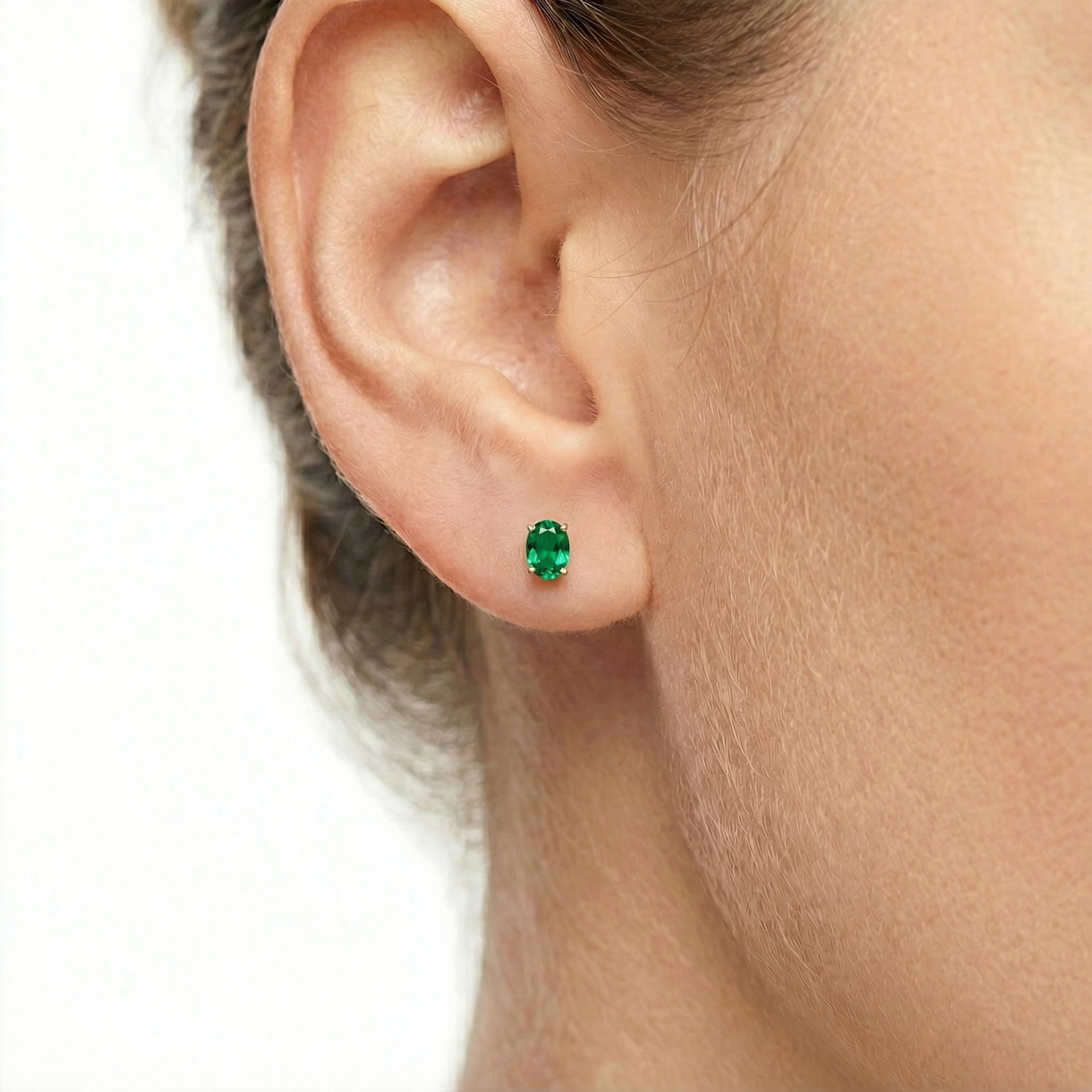 Close-up of an oval cut simulated emerald stud earring in 18K gold vermeil worn on a model's ear.