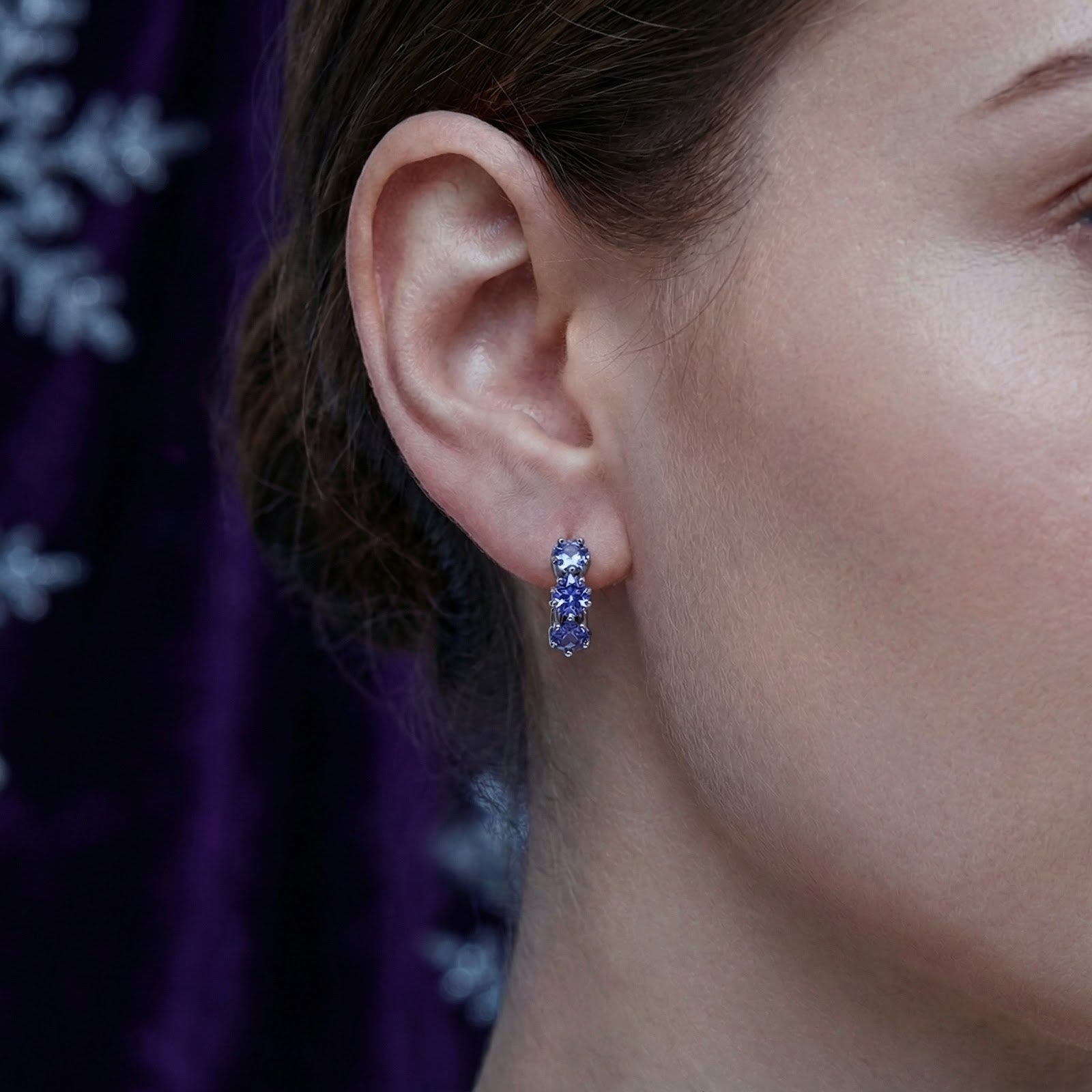 Close-up of a woman wearing a sterling silver star huggie earring with blue simulated tanzanite stones.