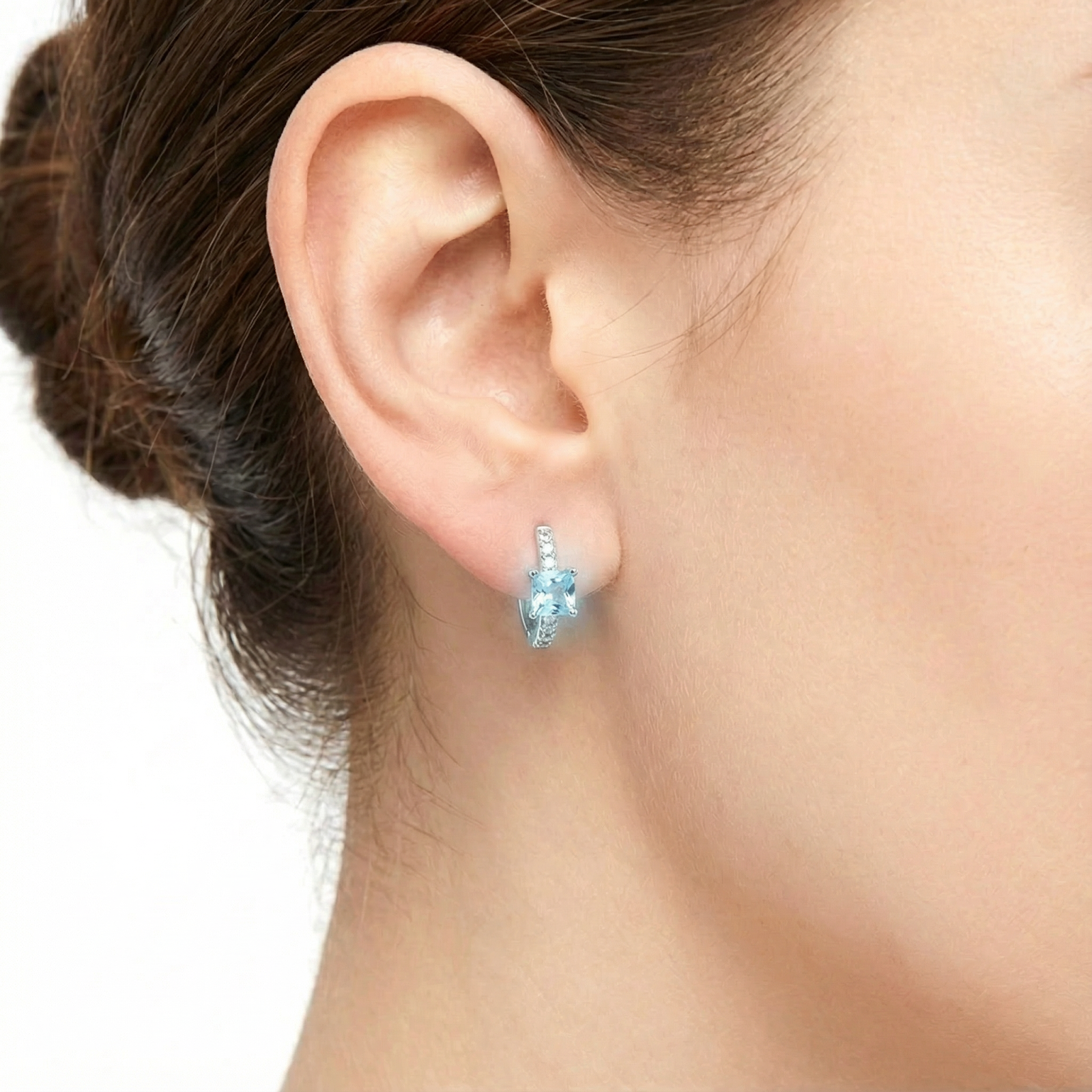 Close-up of a model wearing a silver Aira huggie earring featuring a square-cut light blue simulated aquamarine.