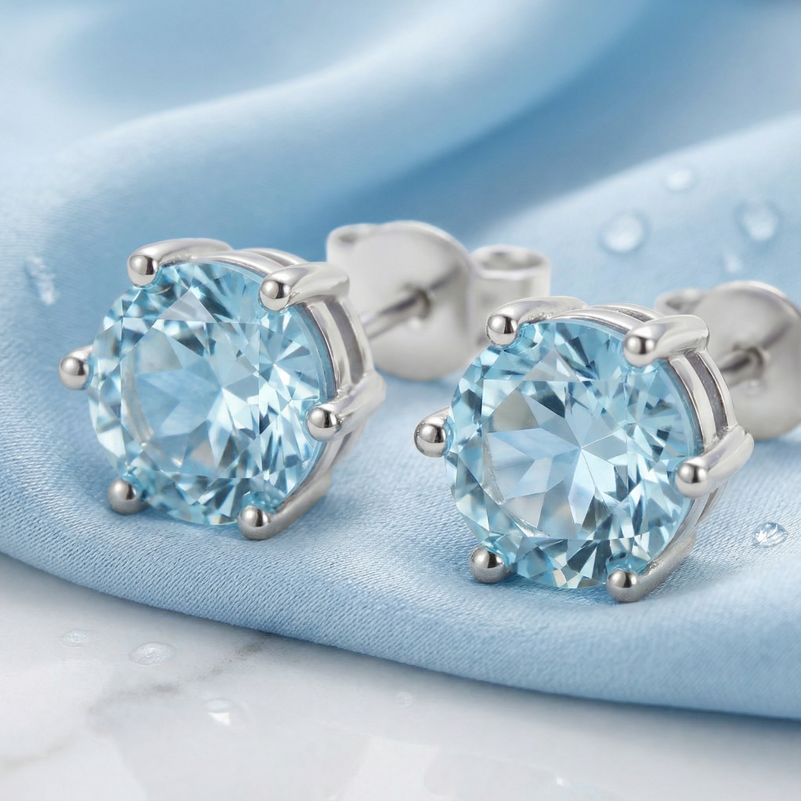 Macro view of round cut simulated aquamarine studs highlighting the brilliant facets and 6-prong silver setting.