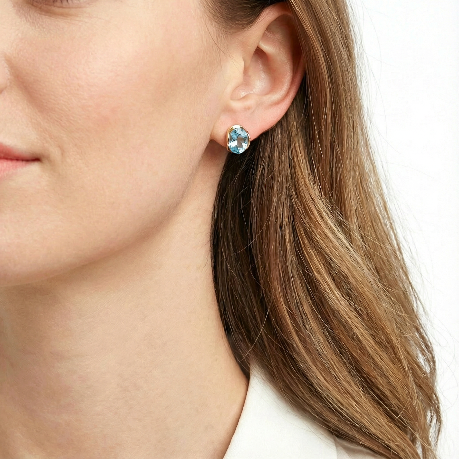 Side view of a woman wearing 18K gold vermeil huggie earrings featuring oval-cut simulated aquamarine stones.