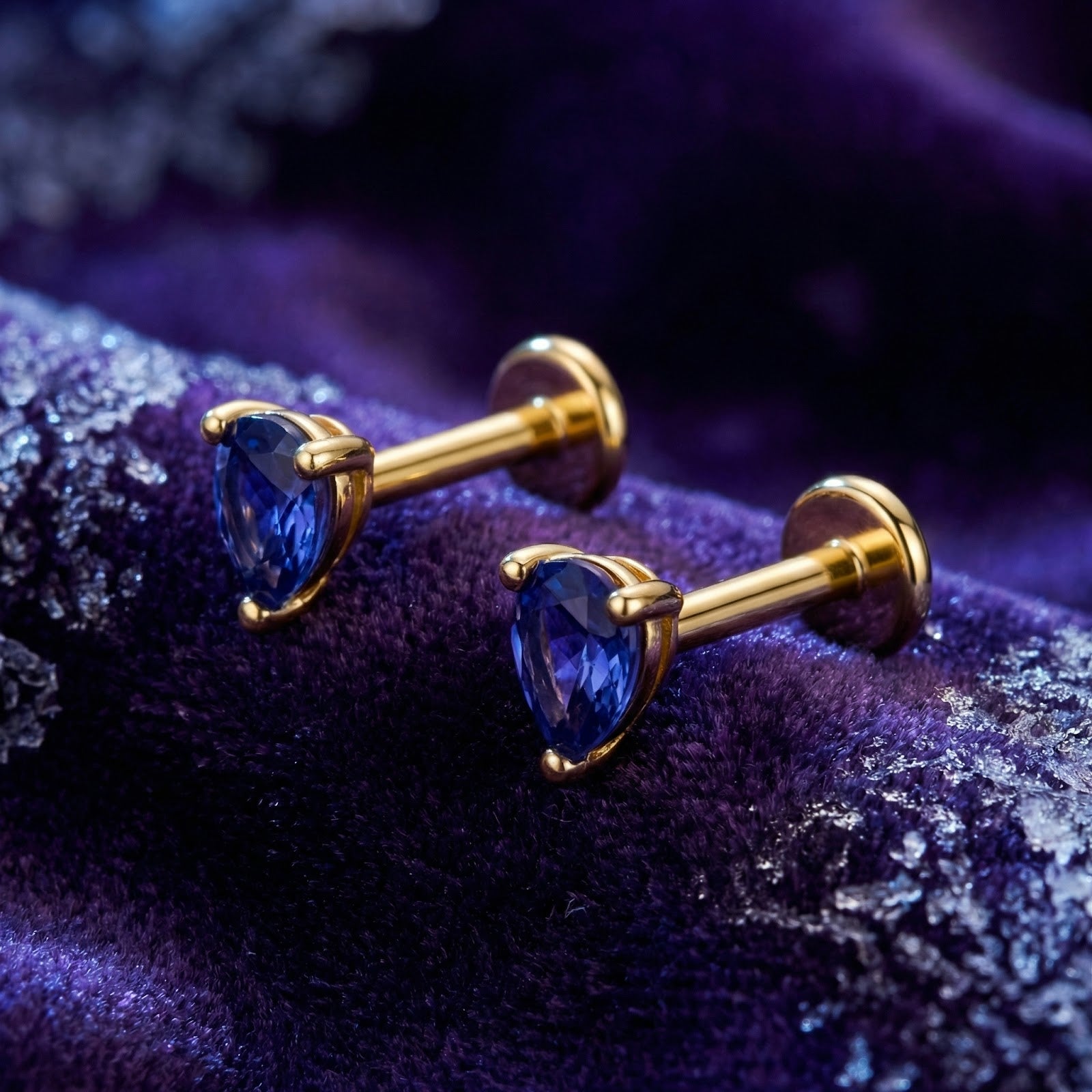 Pear-cut simulated tanzanite earrings in 18K gold vermeil on a purple velvet background with winter accents.