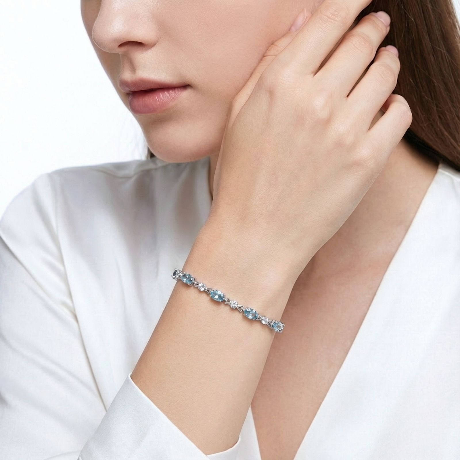 Model wearing the silver Melodia bracelet with light blue oval cut simulated aquamarine stones and a white blouse.