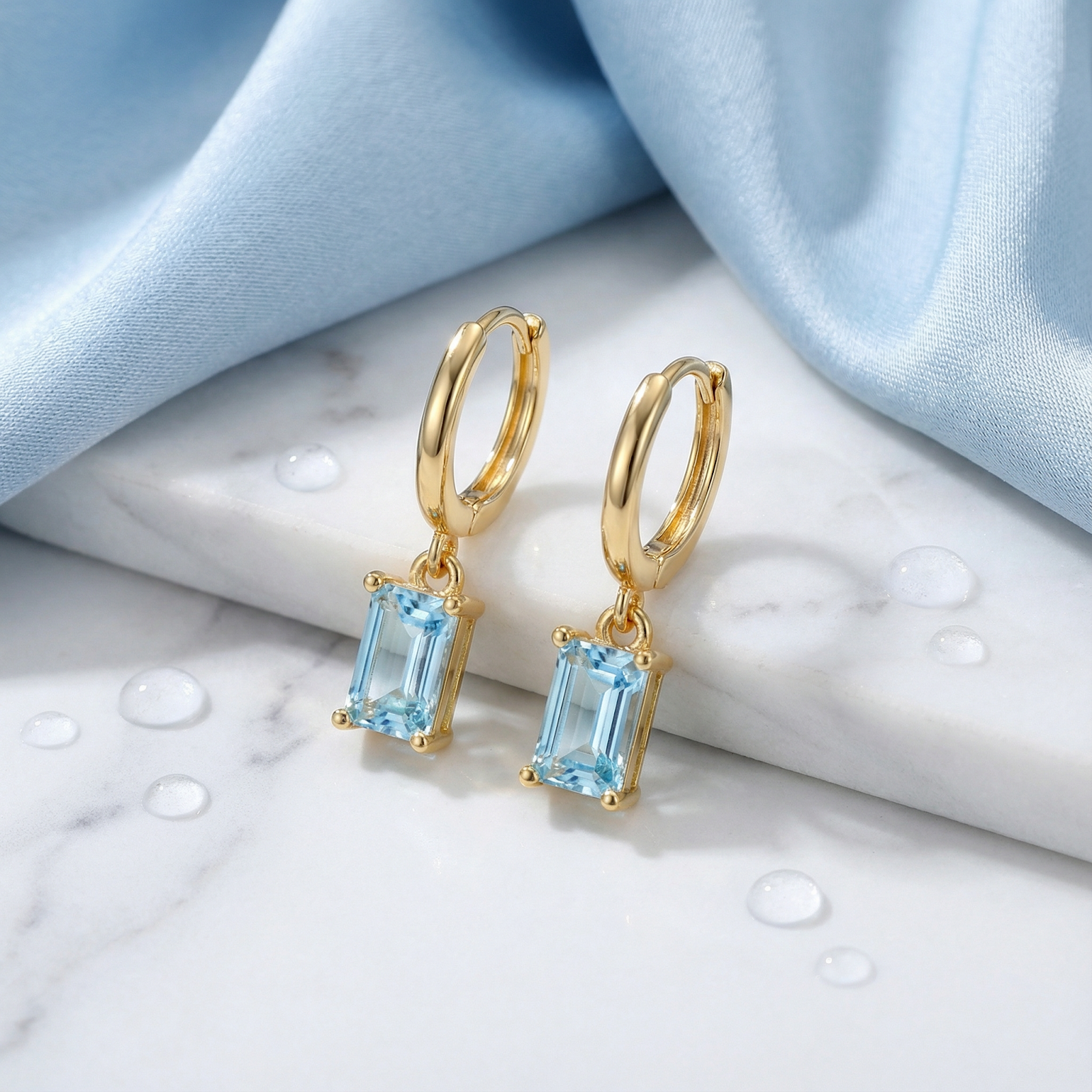 18K gold vermeil hoop earrings with rectangular-cut simulated aquamarine stones on a white marble surface.