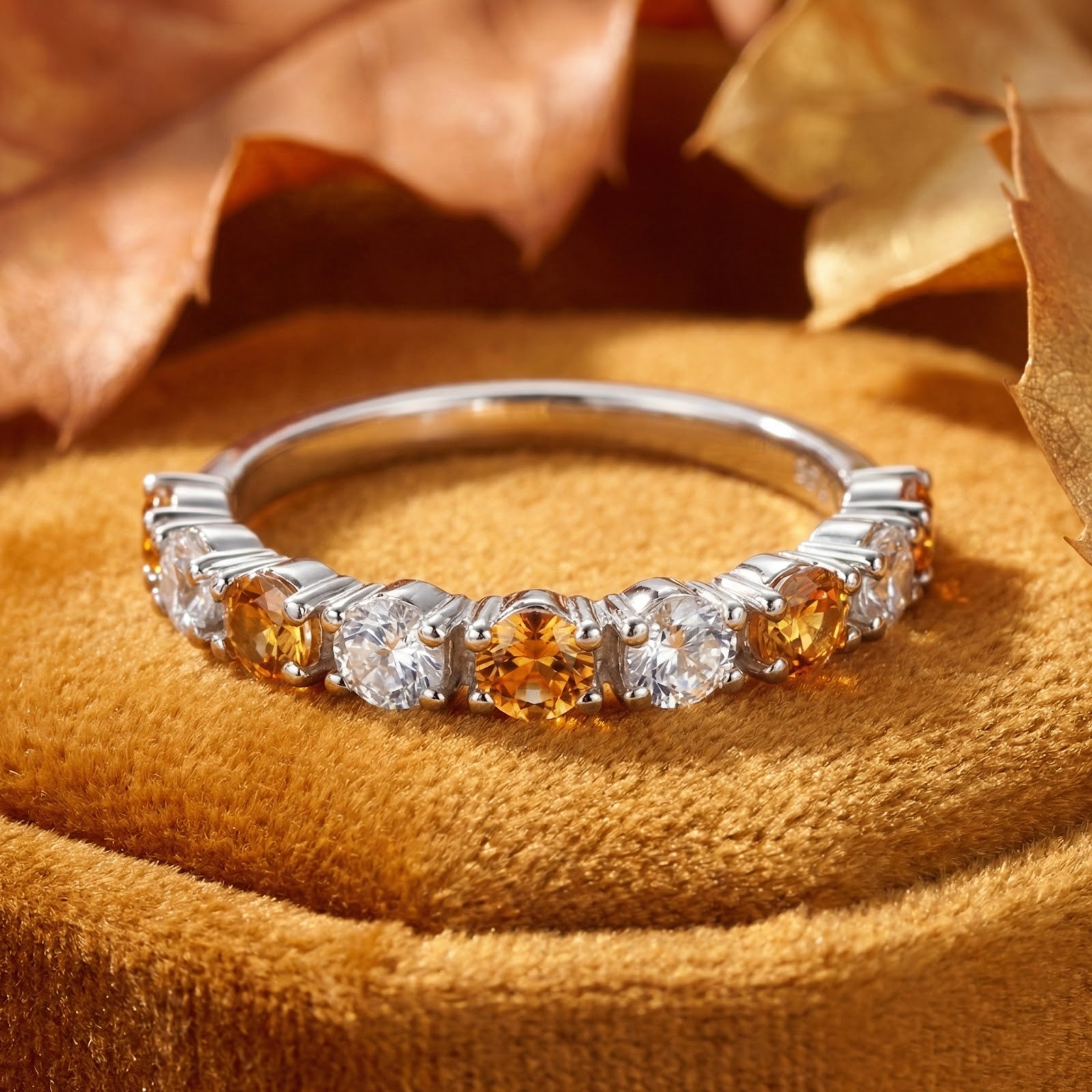 Novara sterling silver half-eternity ring with round honey simulated topaz on yellow velvet with autumn leaves.