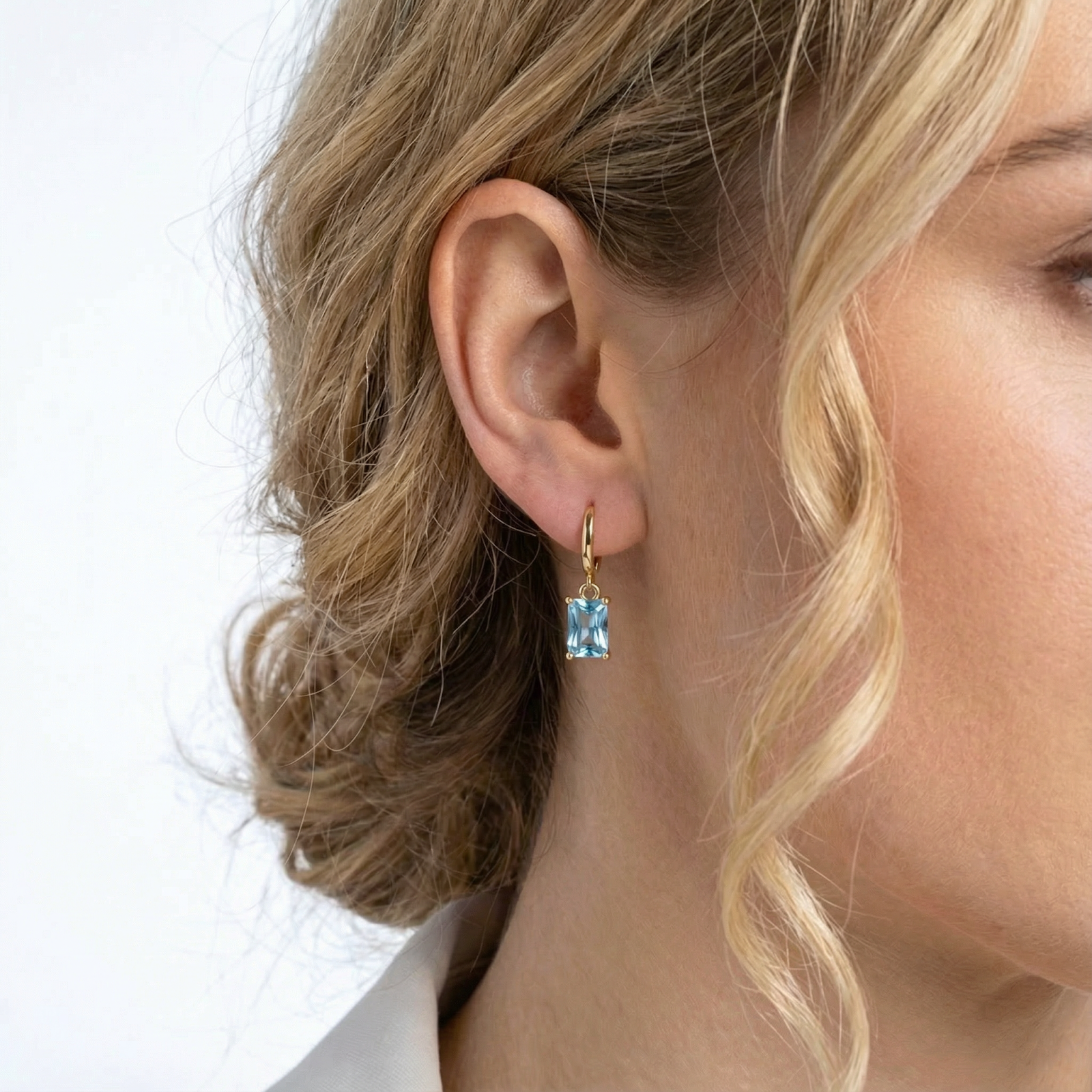 Close-up of a model wearing an 18K gold vermeil hoop earring with a rectangular-cut simulated aquamarine drop.