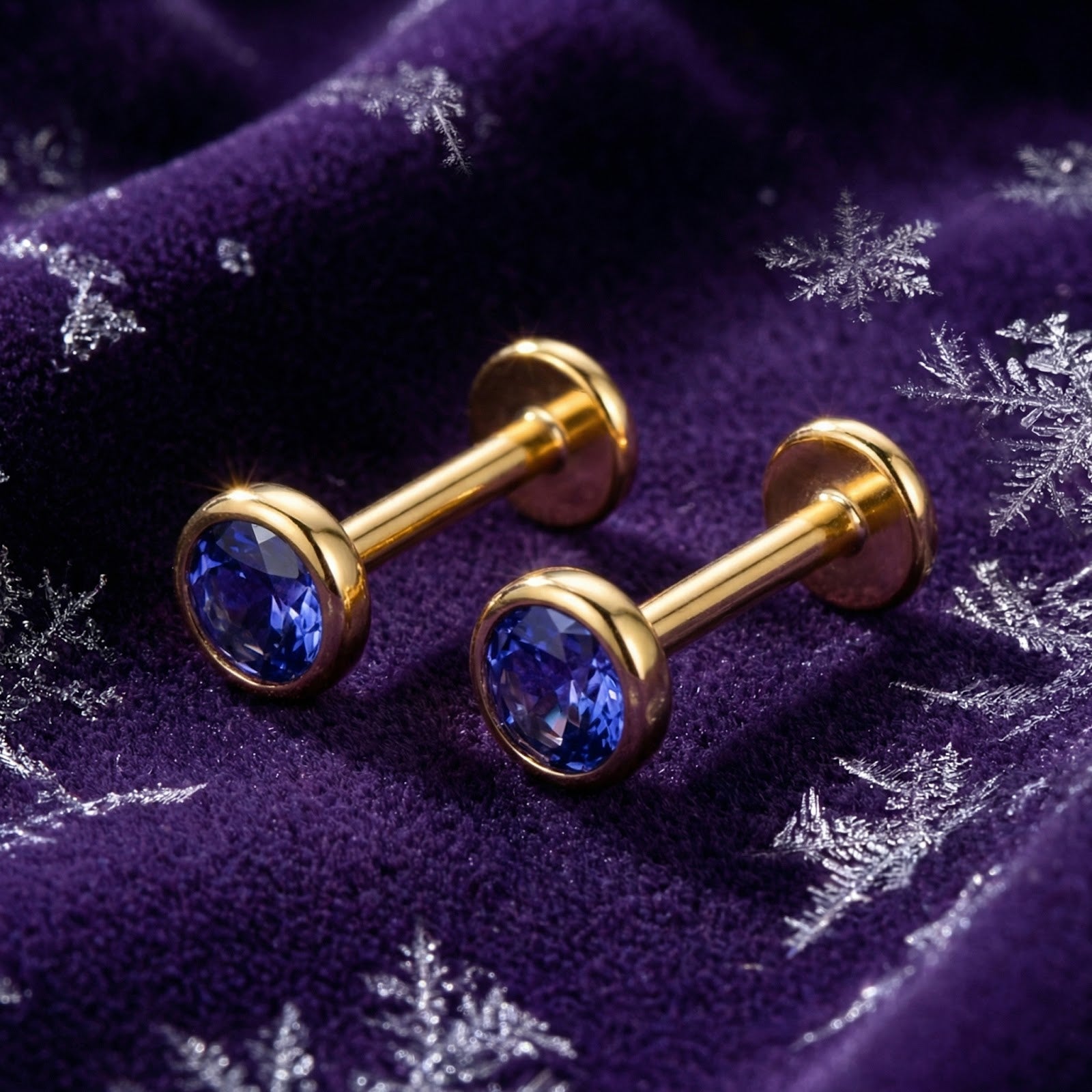 Gold vermeil bezel stud earrings with round simulated tanzanite stones on purple velvet with snowflakes.