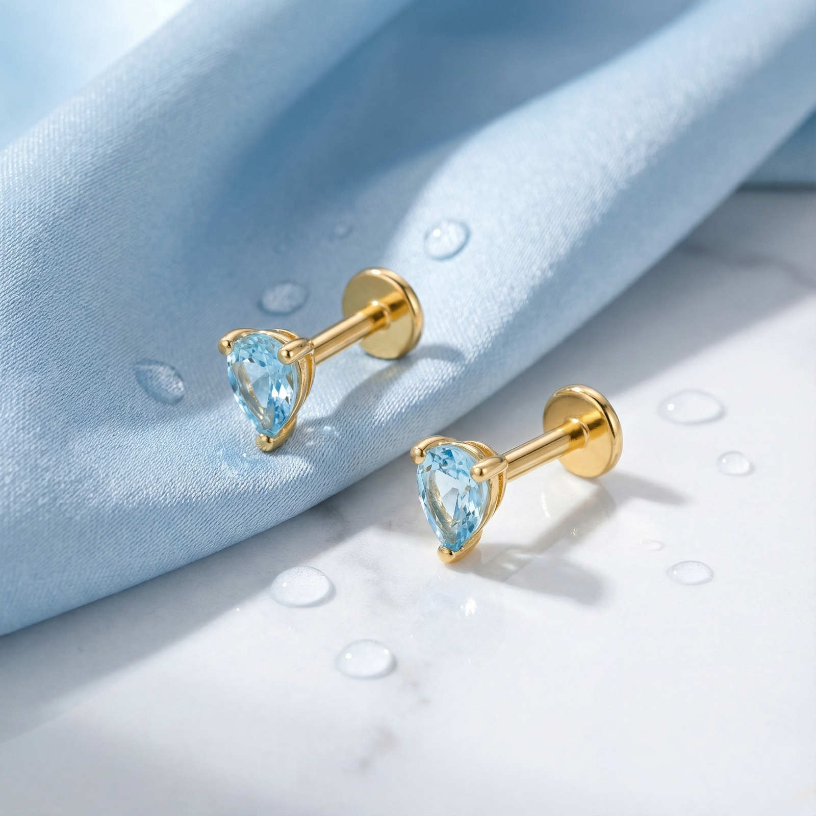 Pear cut simulated aquamarine teardrop earrings in 18K gold vermeil styled on blue fabric and marble.
