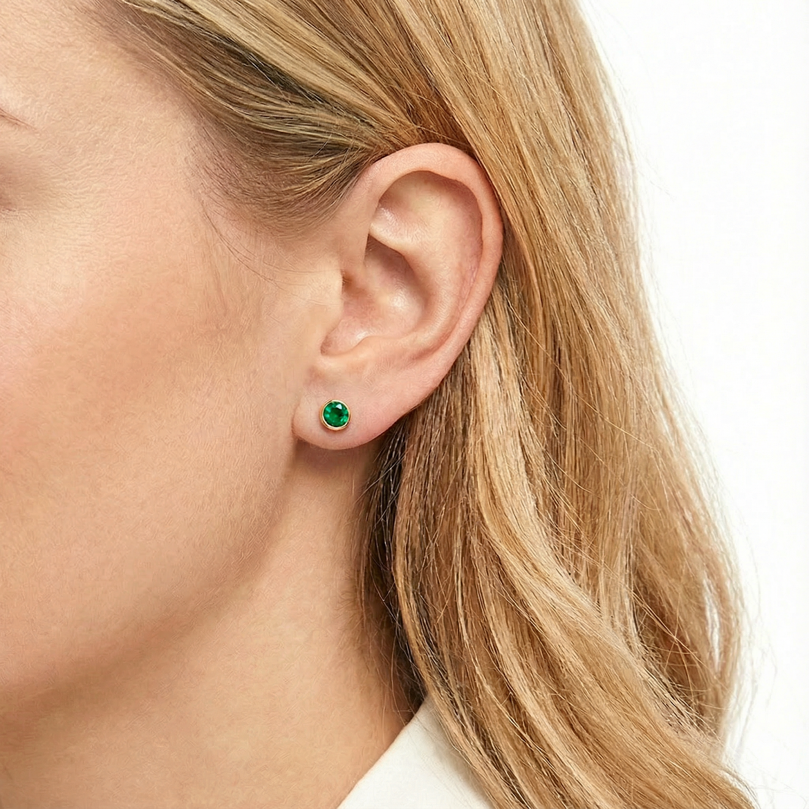 Blonde woman wearing a round simulated emerald bezel stud earring in 18K gold vermeil on her ear.