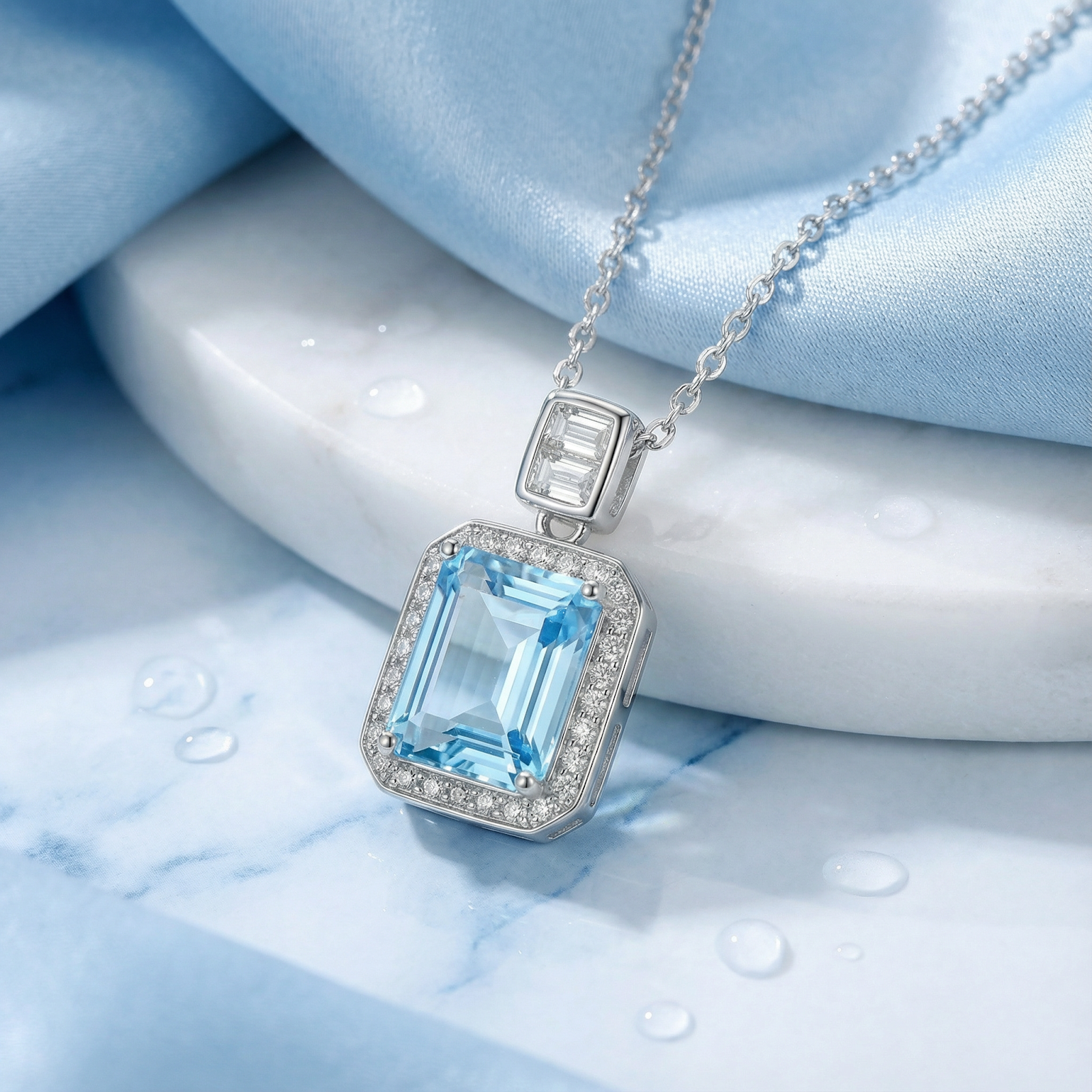 Emerald-cut simulated aquamarine pendant in sterling silver on marble with blue silk and water droplets.