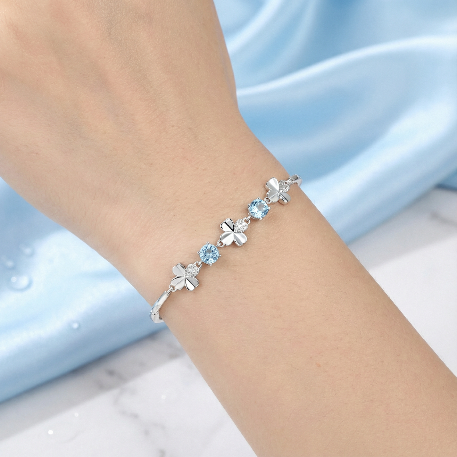 Close-up of round light blue simulated aquamarine stones on a sterling silver clover bracelet worn on a wrist.