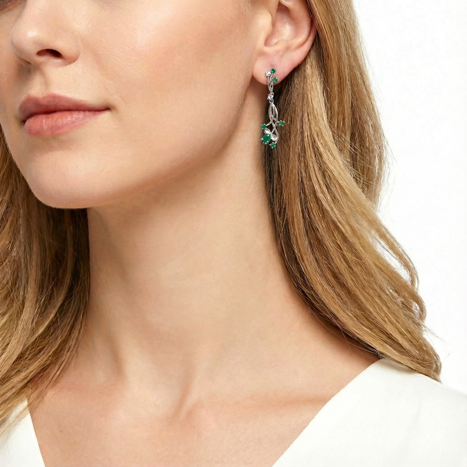Model wearing the Calysia Vine sterling silver drop earrings with vivid green simulated emeralds against a white top.