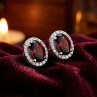Oval cut simulated garnet halo stud earrings in sterling silver on a dark red velvet background.