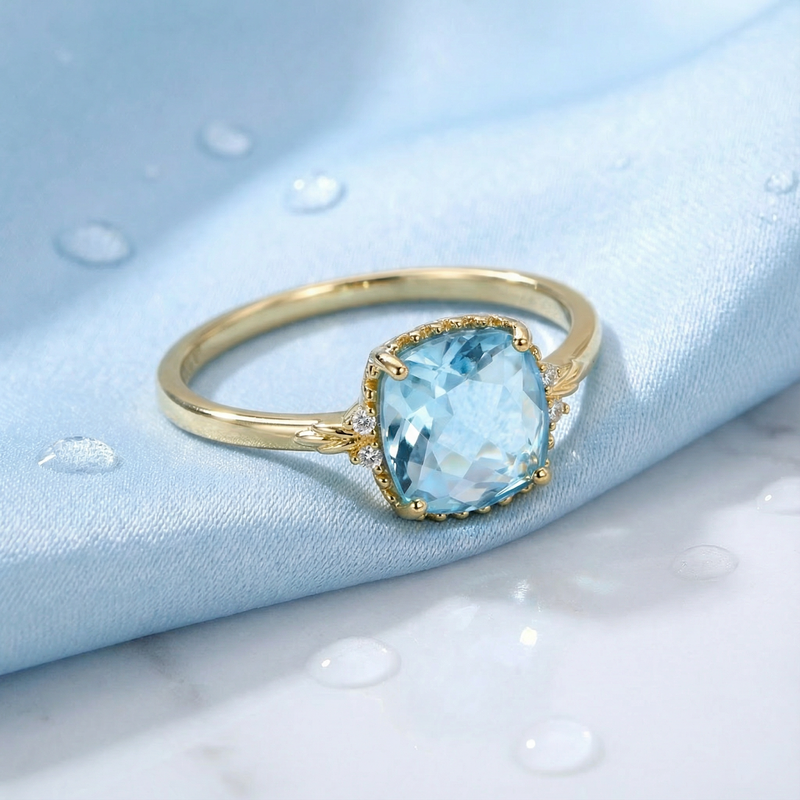 Side view of the Zephyra cushion cut simulated aquamarine ring in 18K gold vermeil on blue fabric.