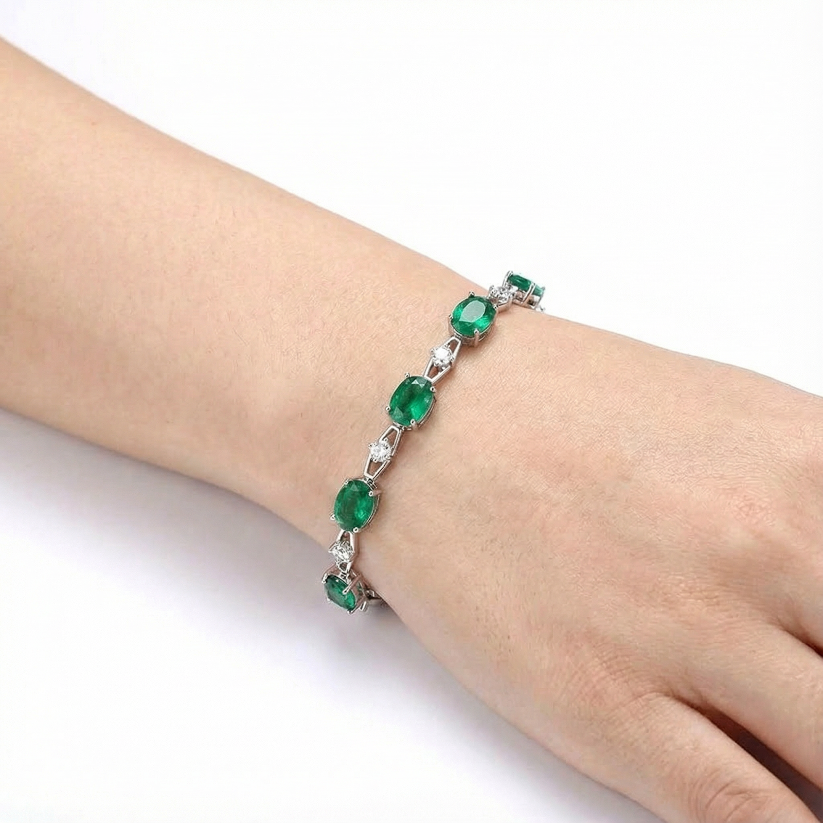 Oval-cut simulated emerald station bracelet in sterling silver shown on a wrist for scale.