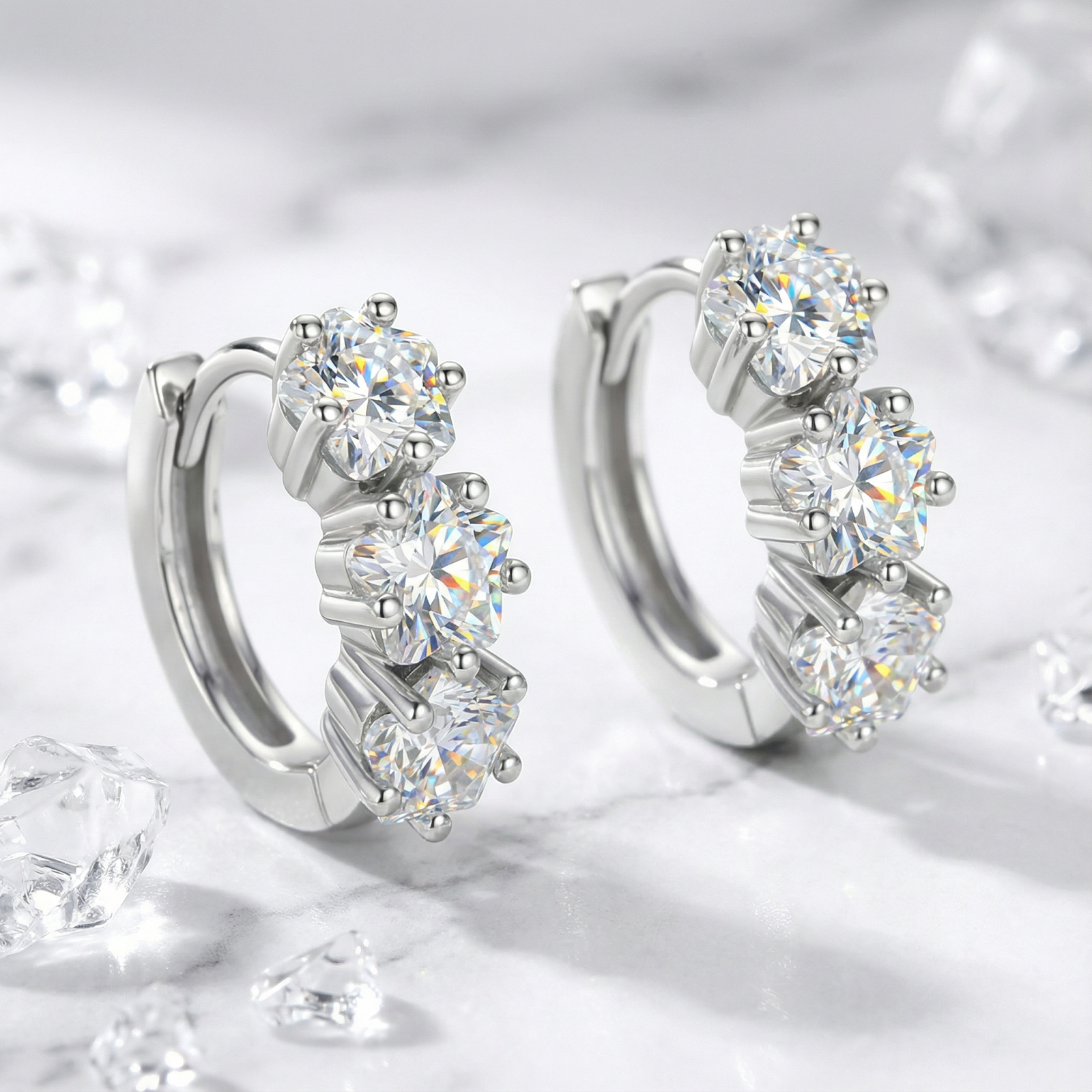 S925 sterling silver huggie earrings with three round-cut simulated diamonds, angled view on marble background.