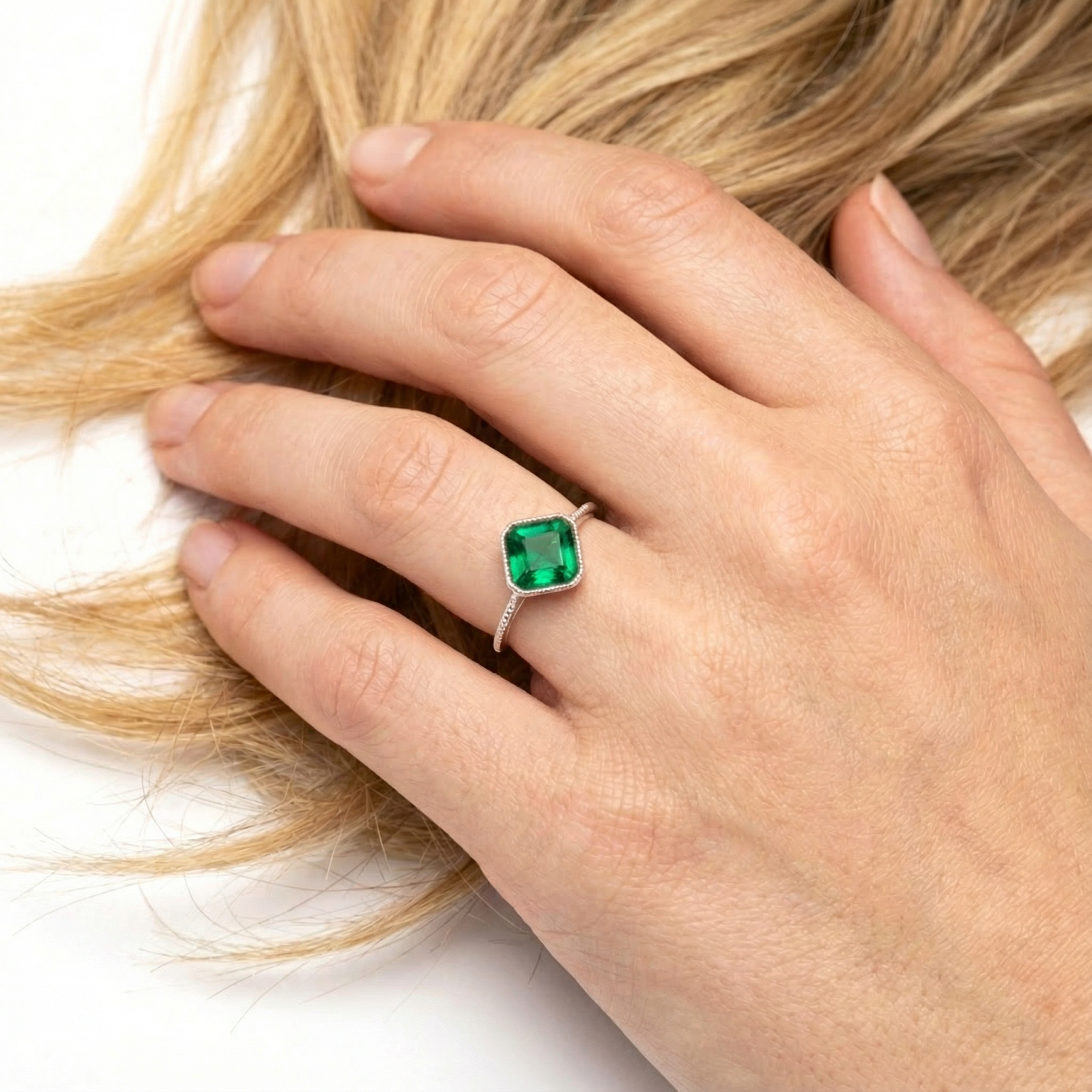 Square-cut simulated emerald ring in S925 sterling silver worn on a hand with blonde hair background.
