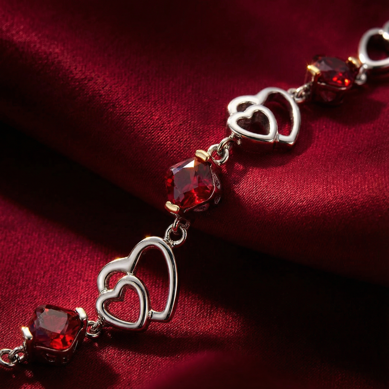 Macro view of sterling silver heart links and precision-cut red simulated rubies on red fabric.