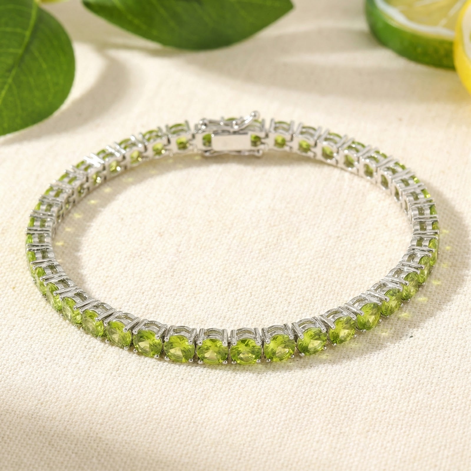 Stainless steel tennis bracelet with round cut simulated peridots laid in a circle with lime slices and leaves.