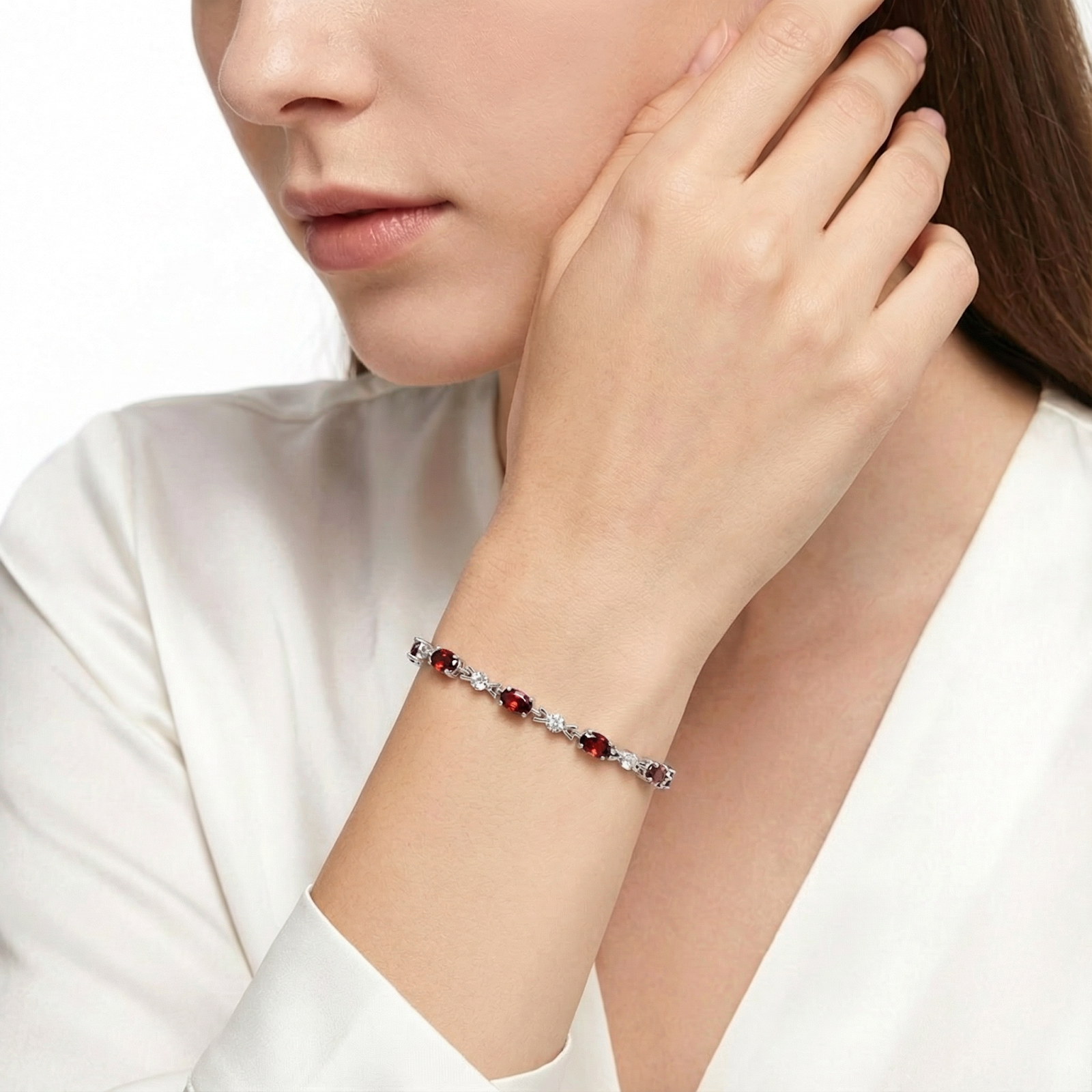 Woman wearing a sterling silver tennis bracelet featuring oval cut simulated red garnets.