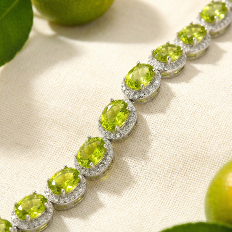 Macro view of oval cut simulated peridot stones in sterling silver halo settings on a tennis bracelet.