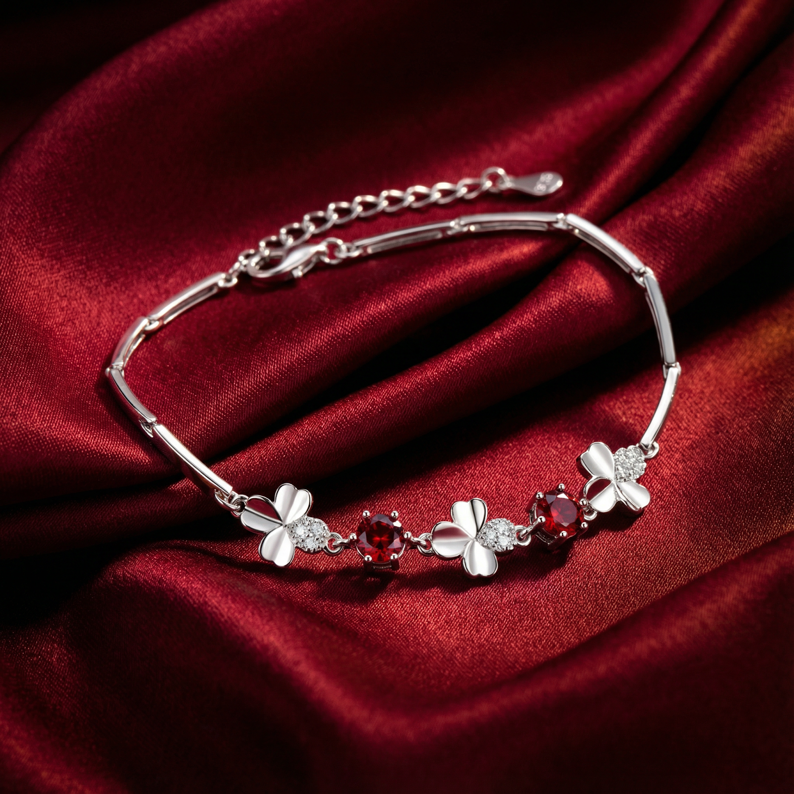 Sterling silver clover bracelet with Pigeon Blood red simulated rubies on red satin fabric.