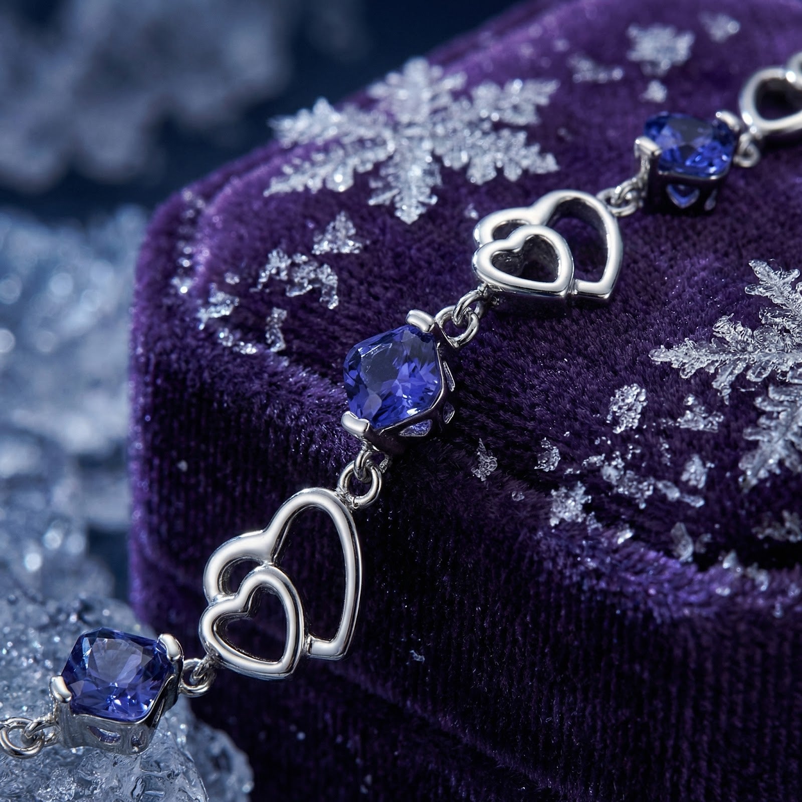 Macro view of S925 sterling silver heart links and cushion-cut blue simulated tanzanite stones on purple velvet.