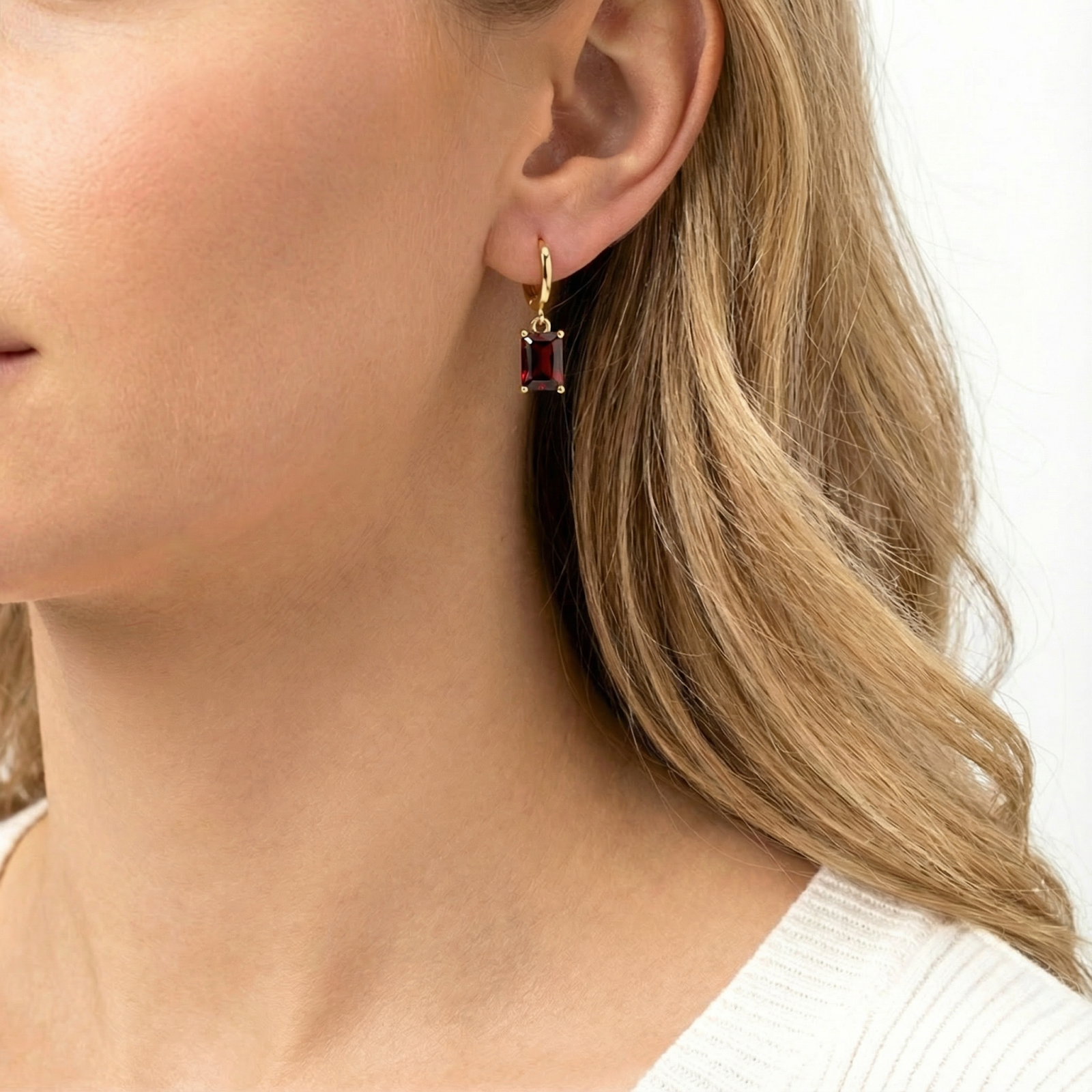 Woman wearing an 18K gold vermeil huggie earring featuring an emerald-cut simulated garnet.