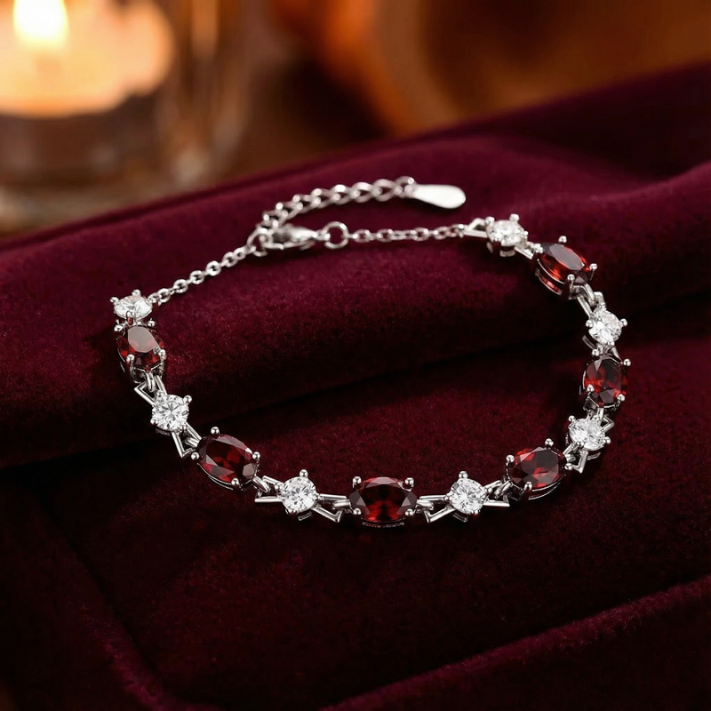 Sterling silver station bracelet with oval red garnets and round white stones on a dark red velvet background.