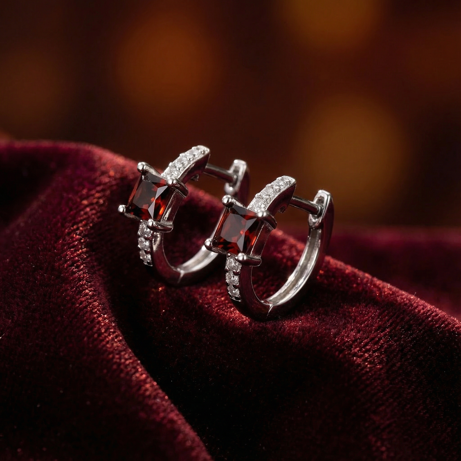 Close-up of princess cut red garnet and sterling silver huggie earrings showing the detailed stone setting.