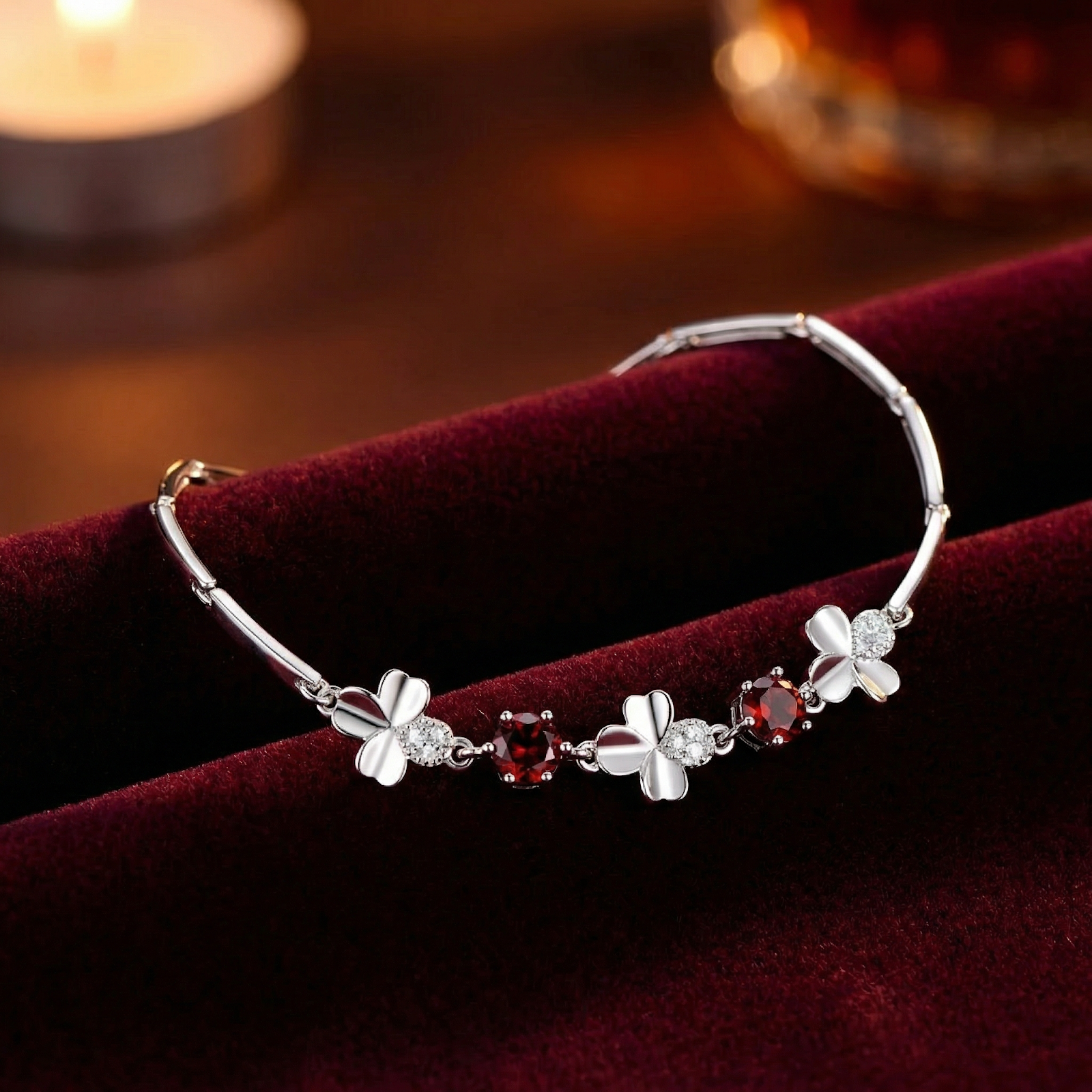 Sterling silver clover bracelet with round-cut red simulated garnets resting on a dark red velvet background.