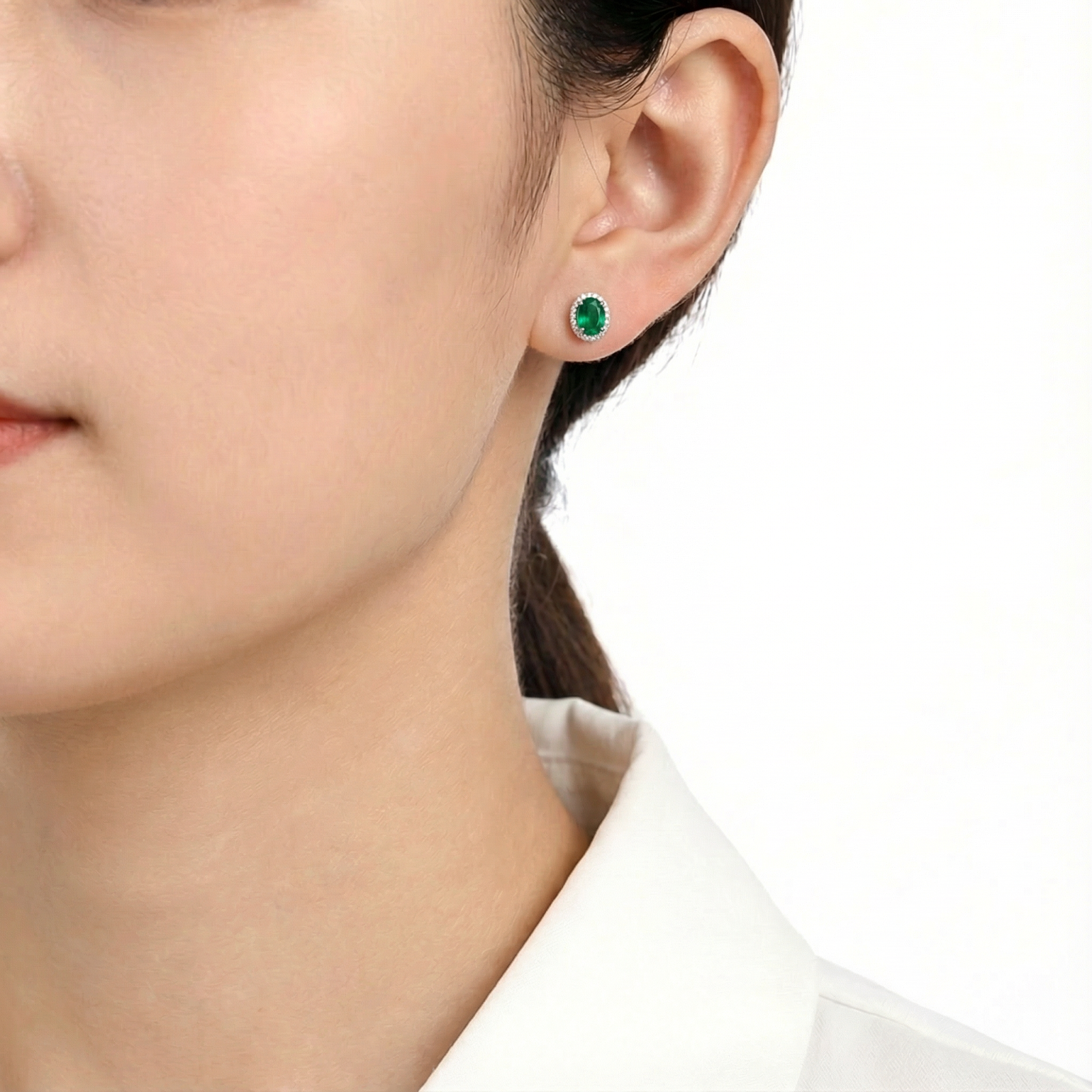 A brunette model wearing an oval simulated emerald halo stud earring in S925 sterling silver on her ear.