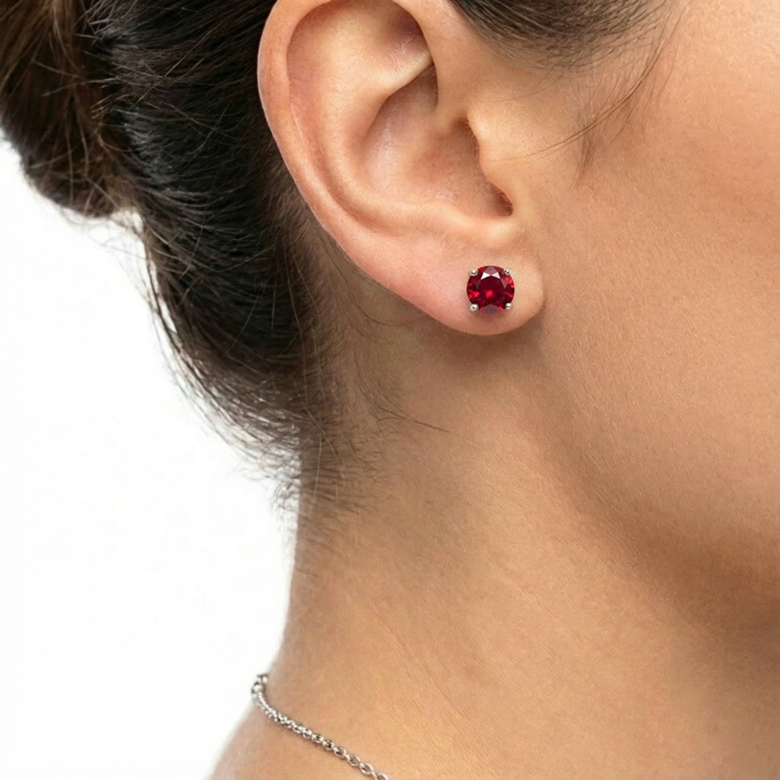 Close-up of a woman wearing a round pigeon blood red simulated ruby stud earring in sterling silver.