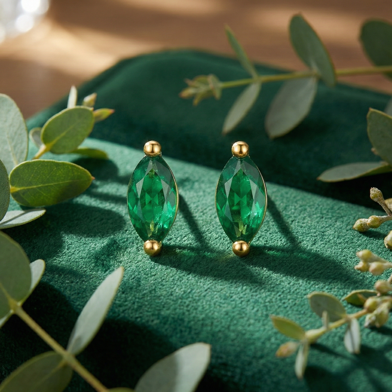 Macro view of marquise-cut simulated emerald stud earrings in 18K gold vermeil on a green velvet background.