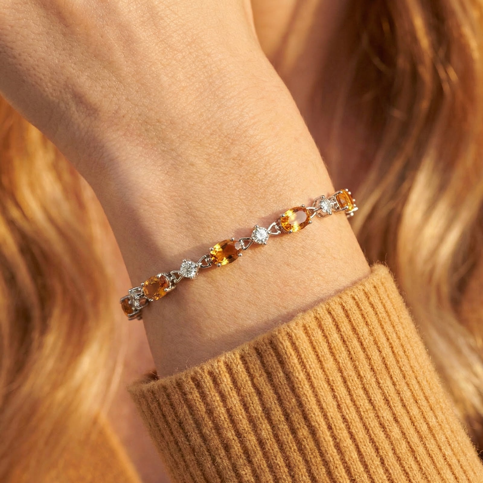 Close-up of oval honeyed topaz and round white stones in a sterling silver bracelet setting on a person's wrist.