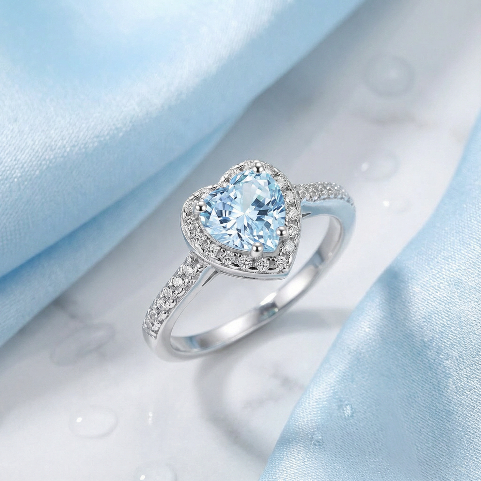 Heart-cut simulated aquamarine sterling silver ring with a halo, styled on blue silk and marble.