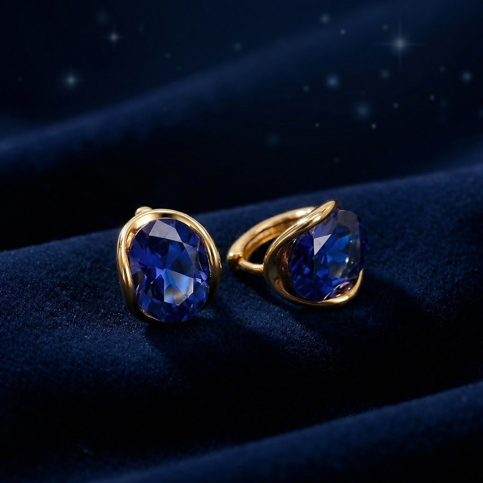 Oval blue simulated sapphire earrings in 18K gold vermeil bezel settings on dark blue velvet.