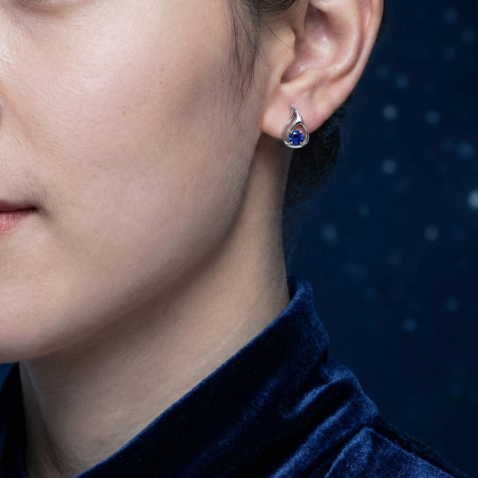 Close-up of a woman wearing a Lysaria Bud sterling silver and royal blue simulated sapphire stud earring.