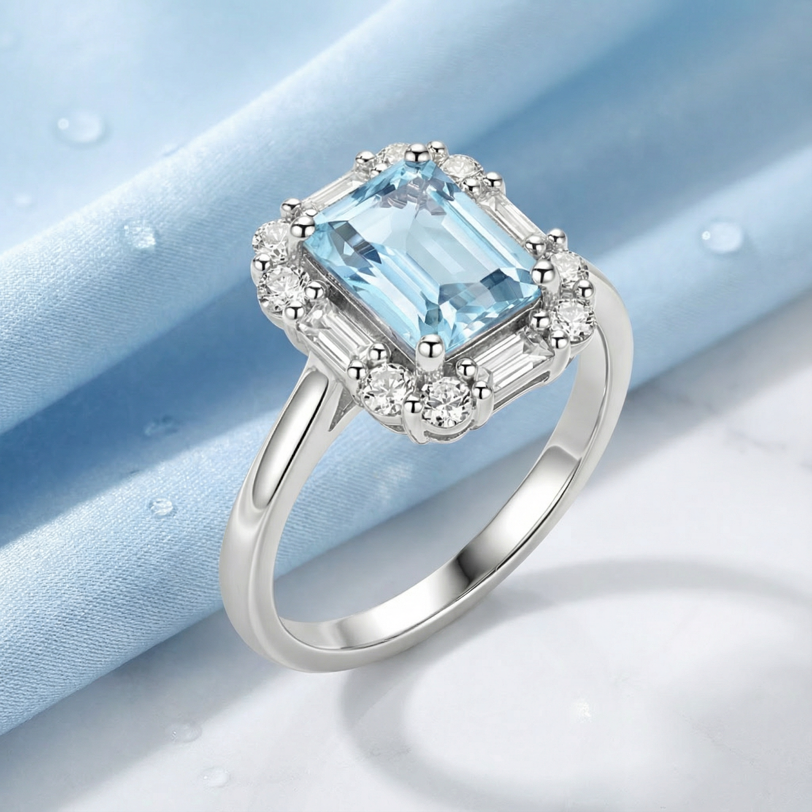 Octagon cut simulated aquamarine halo ring in sterling silver on a light blue silk background with water droplets.