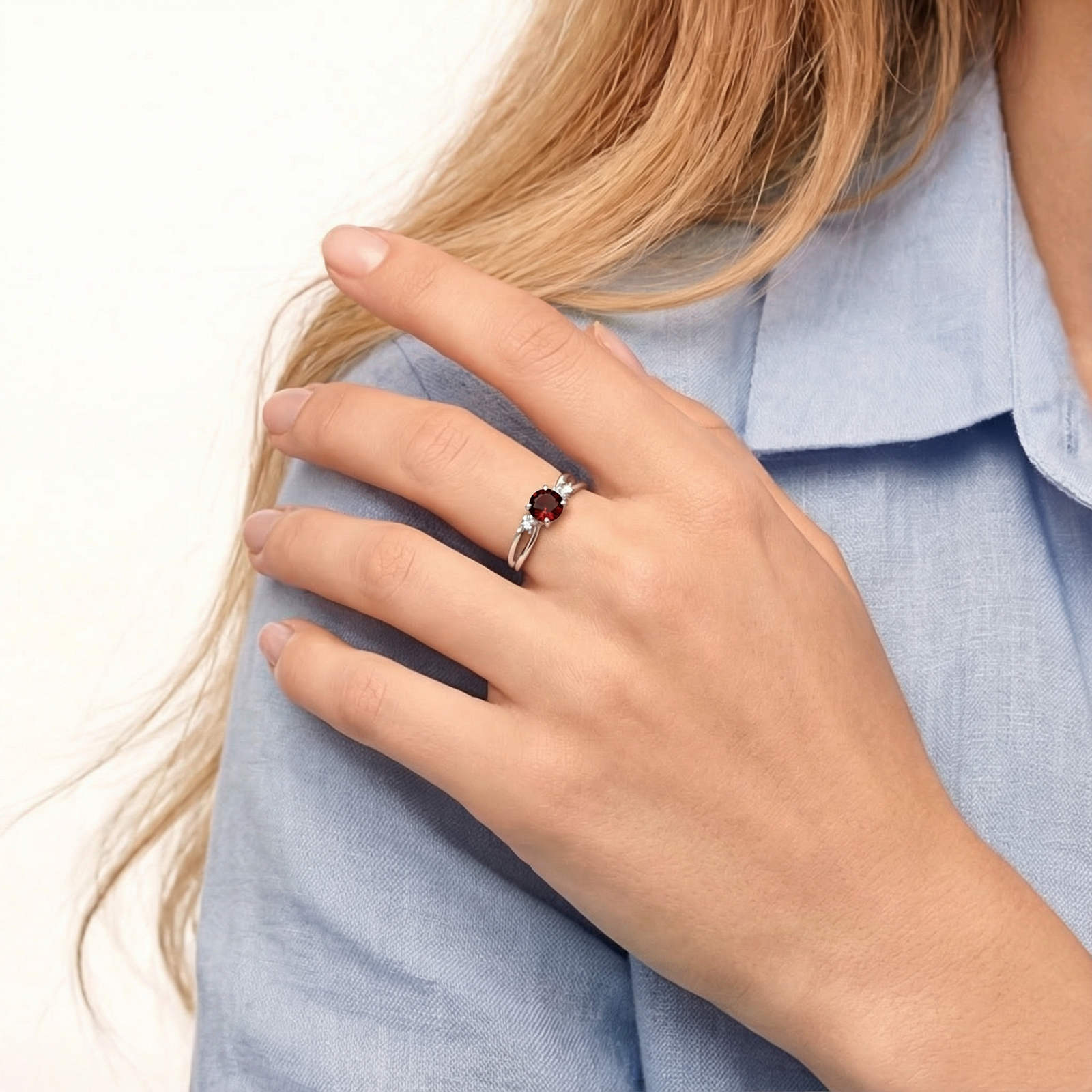 Sterling silver Aeryn bypass ring with a round red simulated garnet worn on a model's hand.