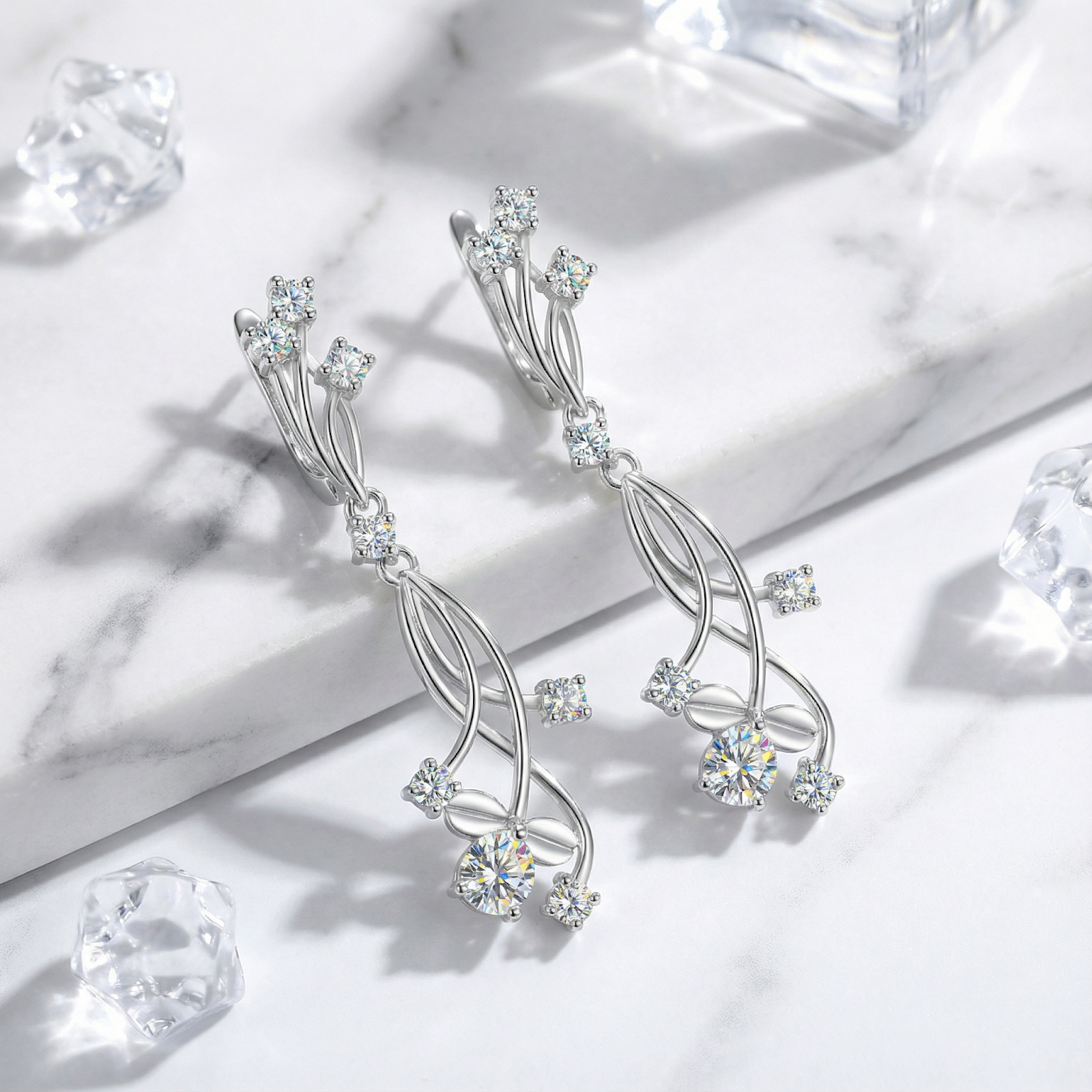 Silver vine drop earrings with round zirconia stones on a marble surface with decorative ice cubes.