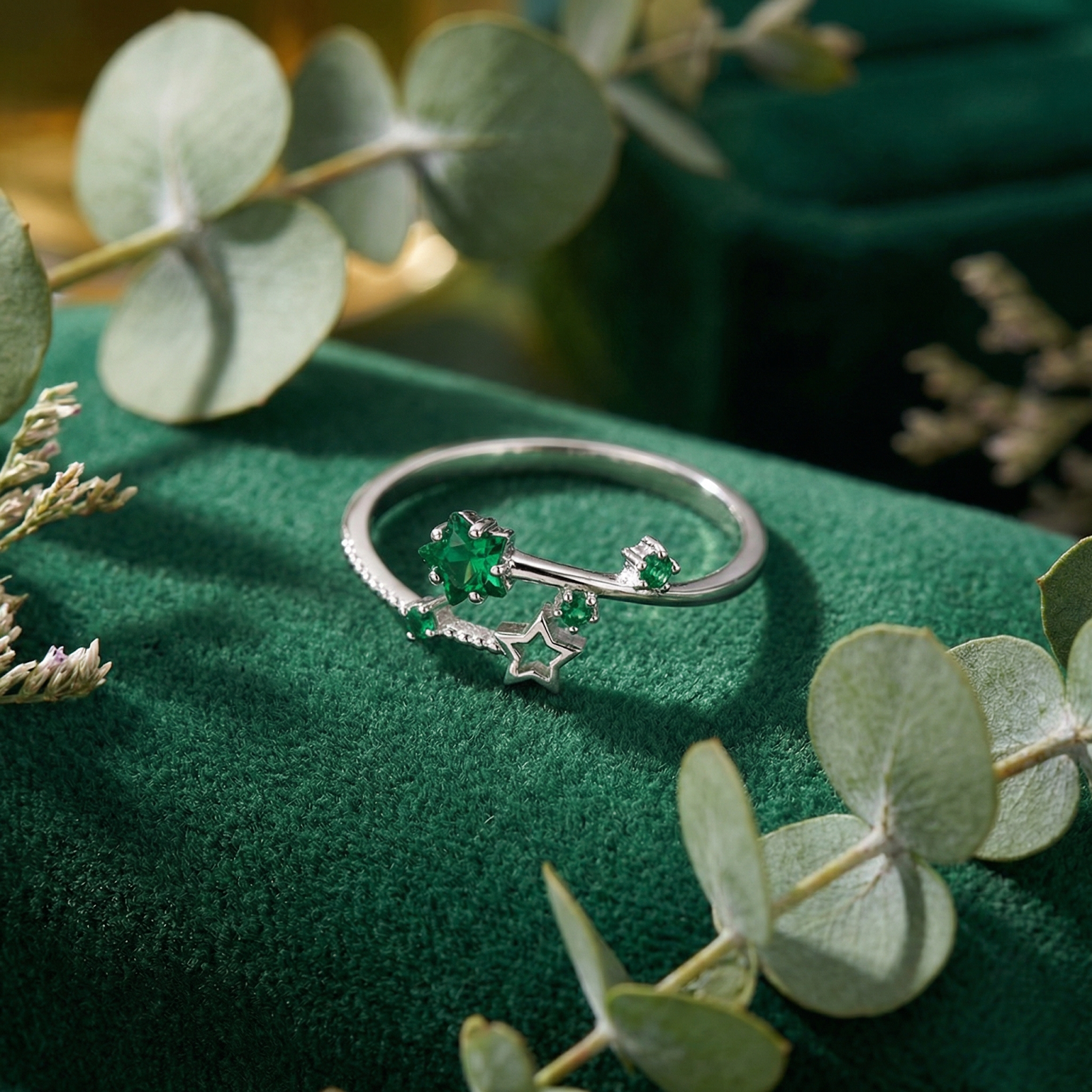 Adjustable silver star ring featuring green simulated emeralds displayed on a green velvet surface with leaves.