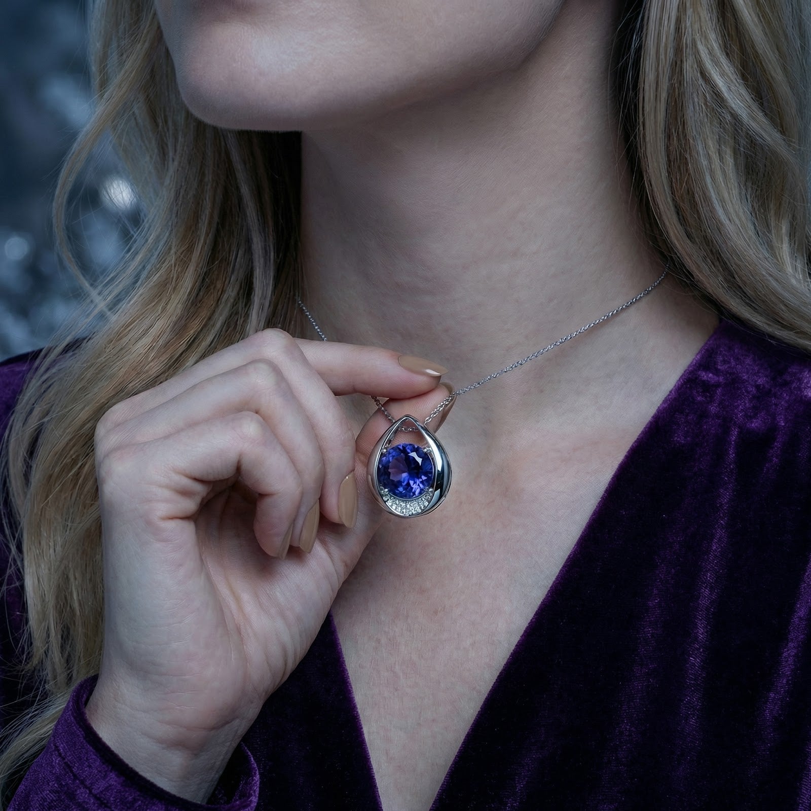 Hand holding the teardrop sterling silver pendant with a round blue simulated tanzanite to show scale on a model.