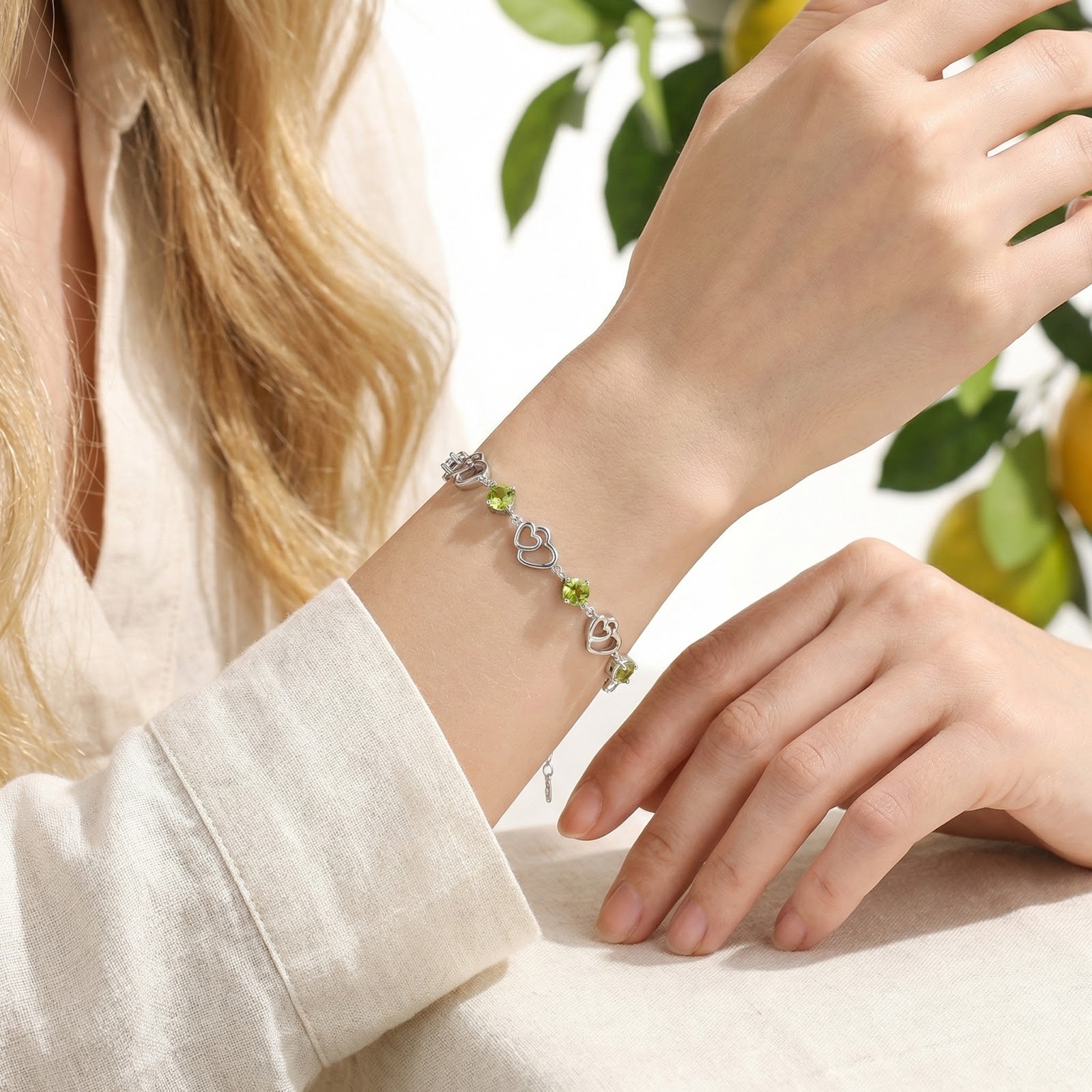 Sterling silver heart bracelet with square-cut simulated peridot stones worn on a woman's wrist.