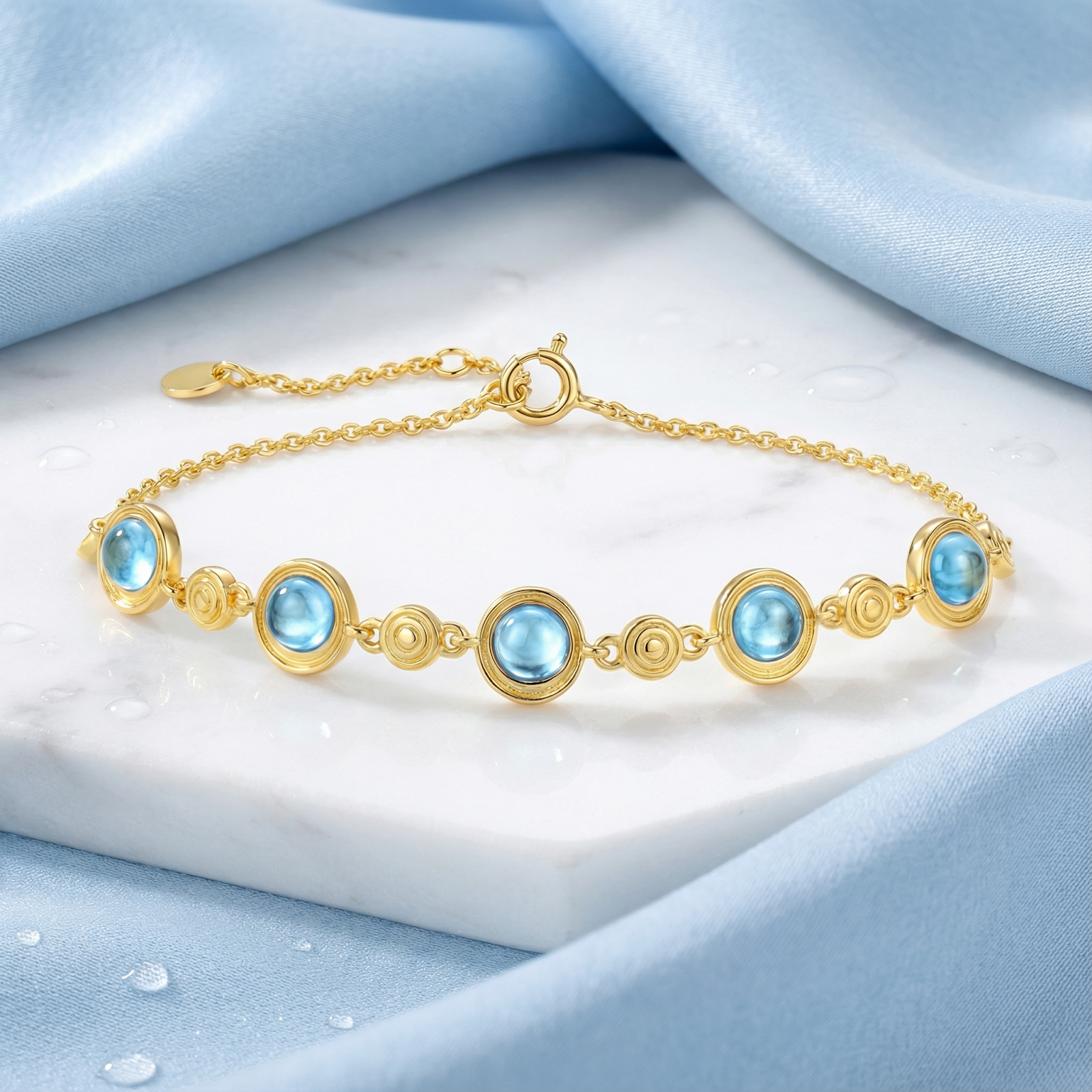 The Marisol 18K gold vermeil station bracelet with five round simulated aquamarine stones on a marble surface.