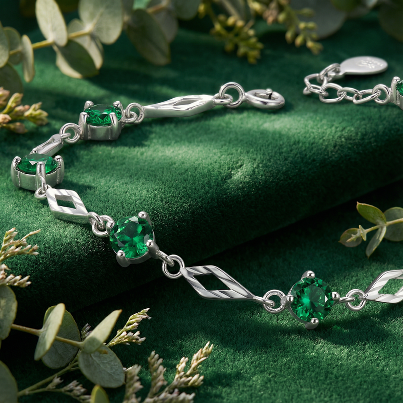 Close-up of round simulated emeralds in sterling silver settings on a green velvet station bracelet.