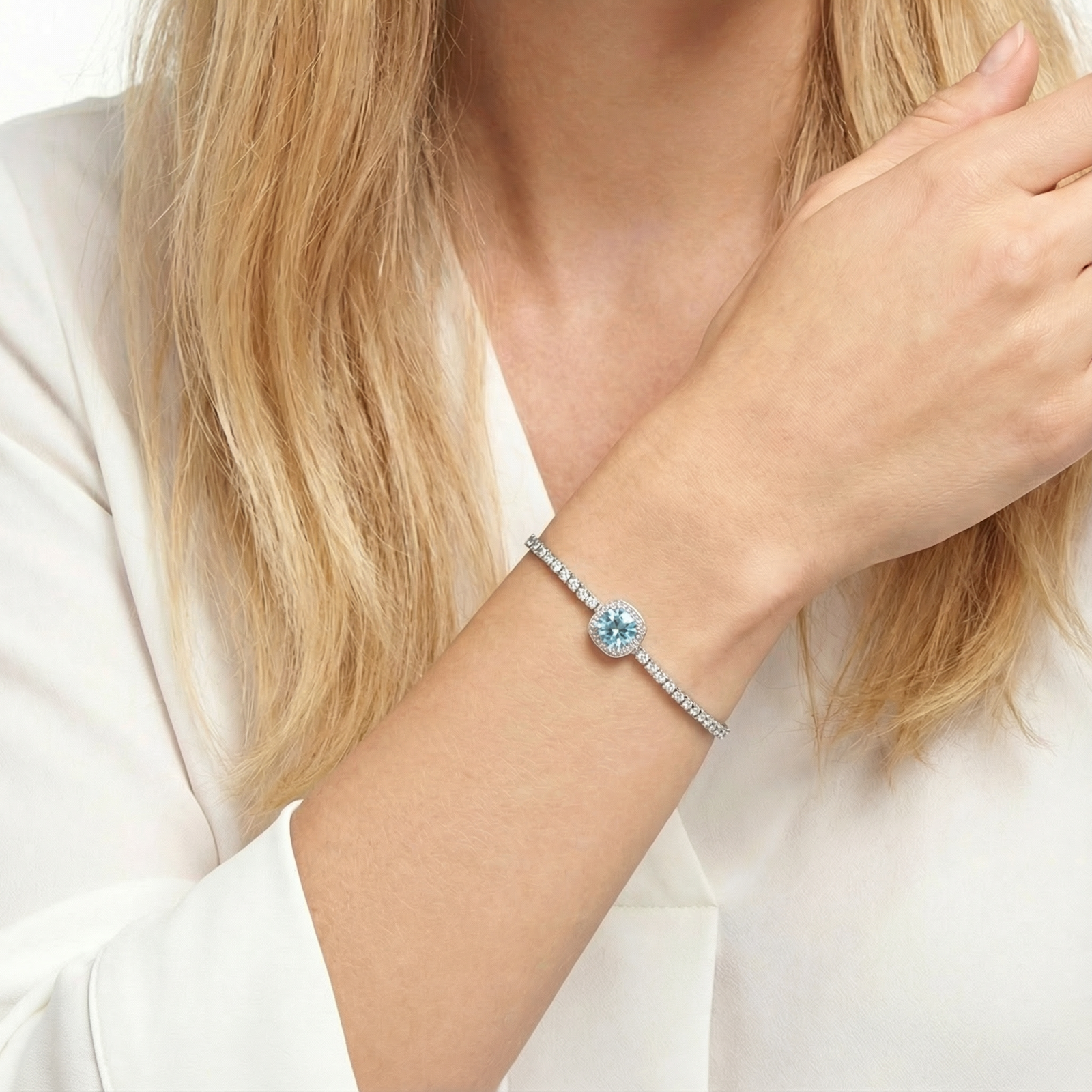 Sterling silver tennis-style halo bracelet with a round blue simulated aquamarine worn on a woman's wrist.